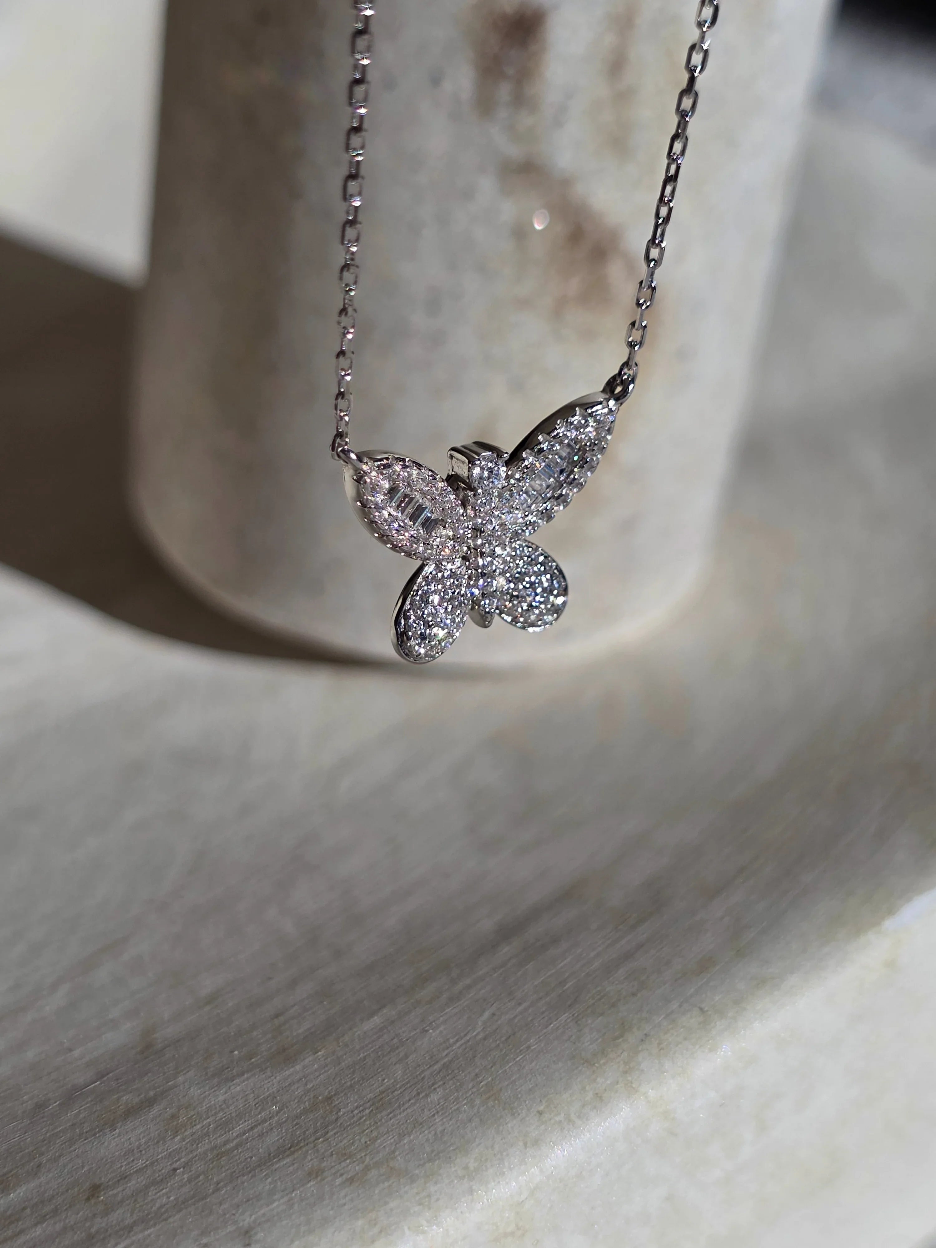 Butterfly-shaped diamond necklace on a marble surface- side