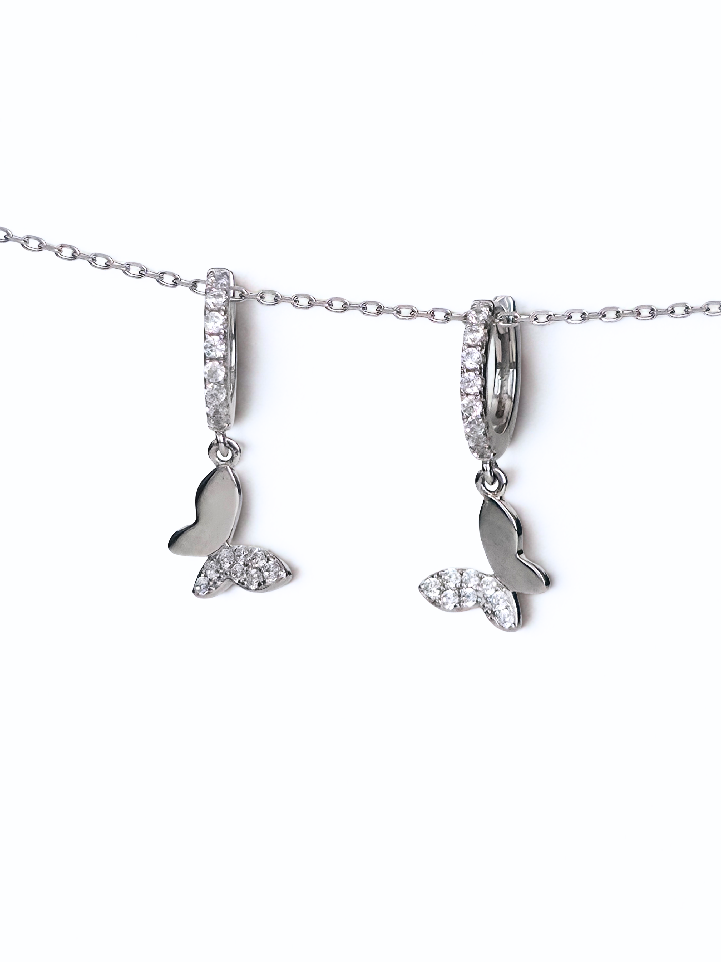 Silver necklace with a butterfly huggieson a white background- further