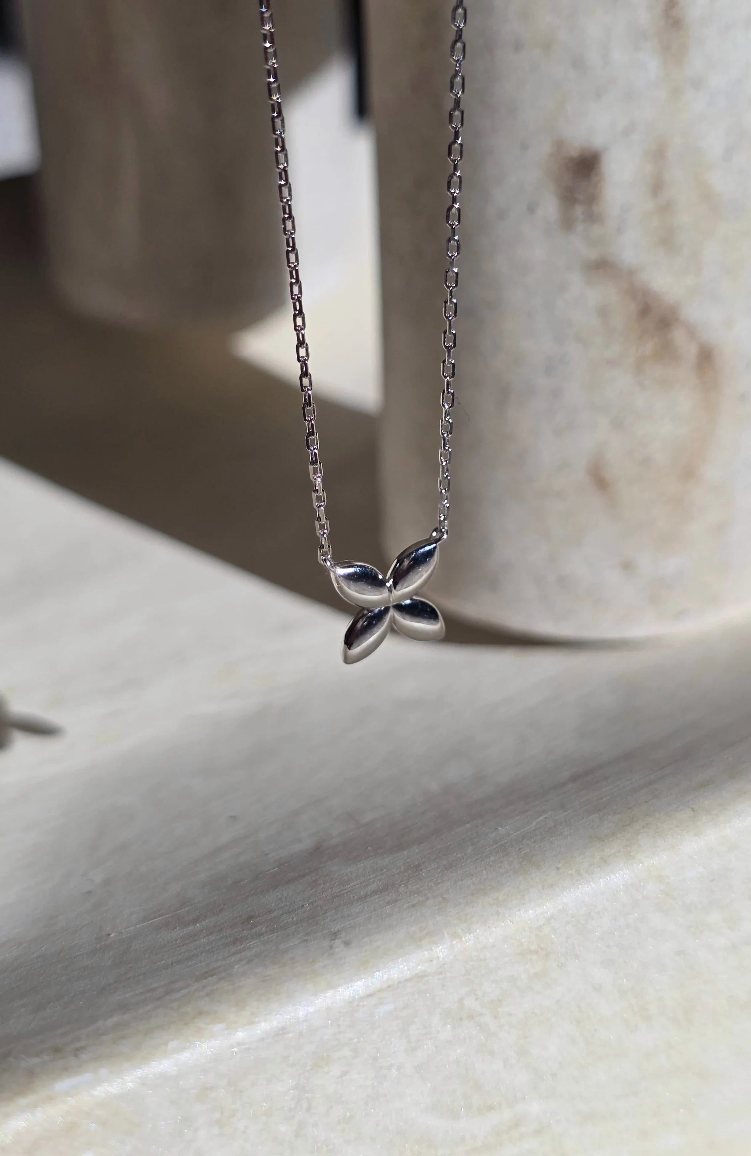 Silver necklace with a butterfly pendant on a light stone surface- side ways- close up