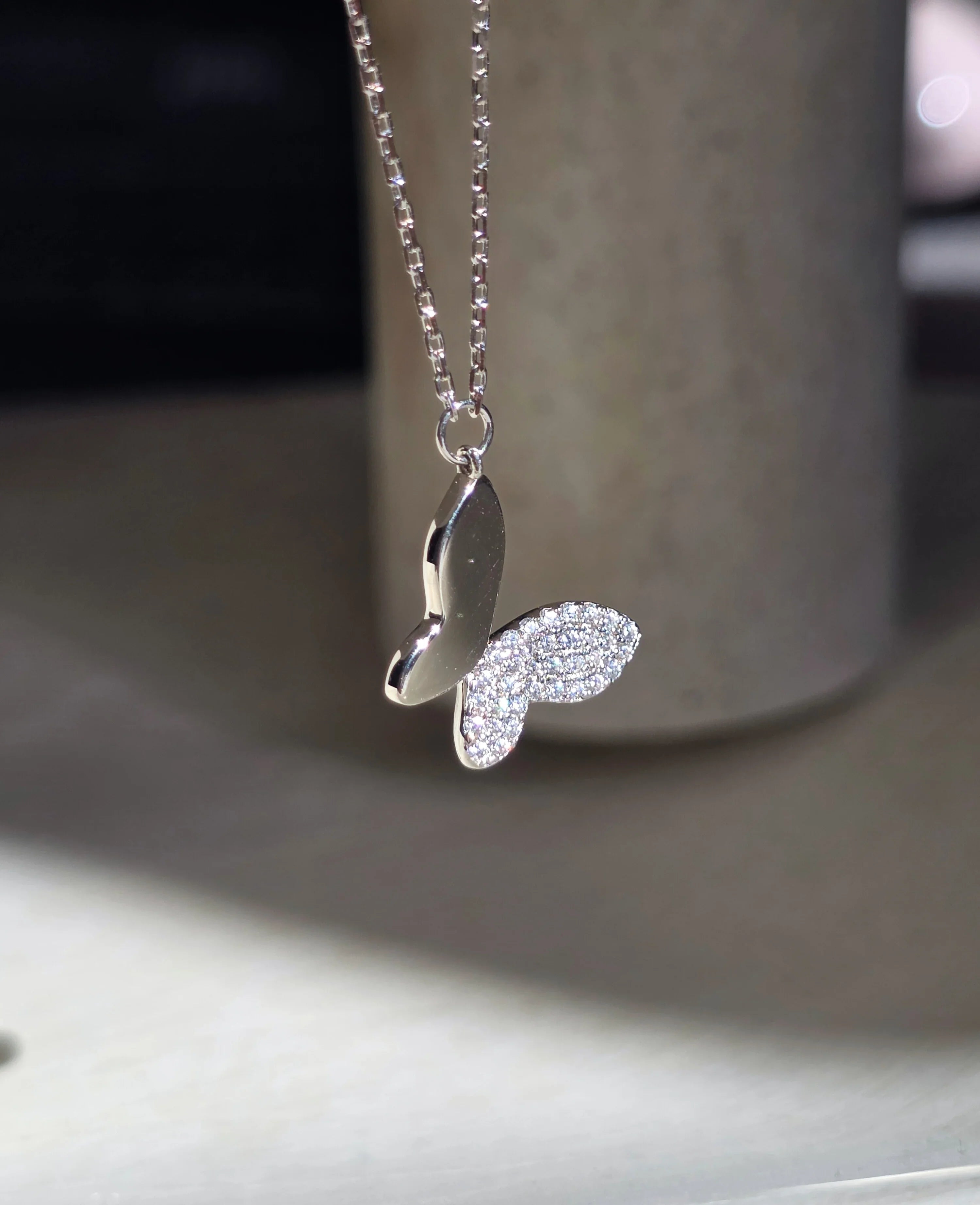 Silver necklace with a butterfly pendant on a neutral background- side ways