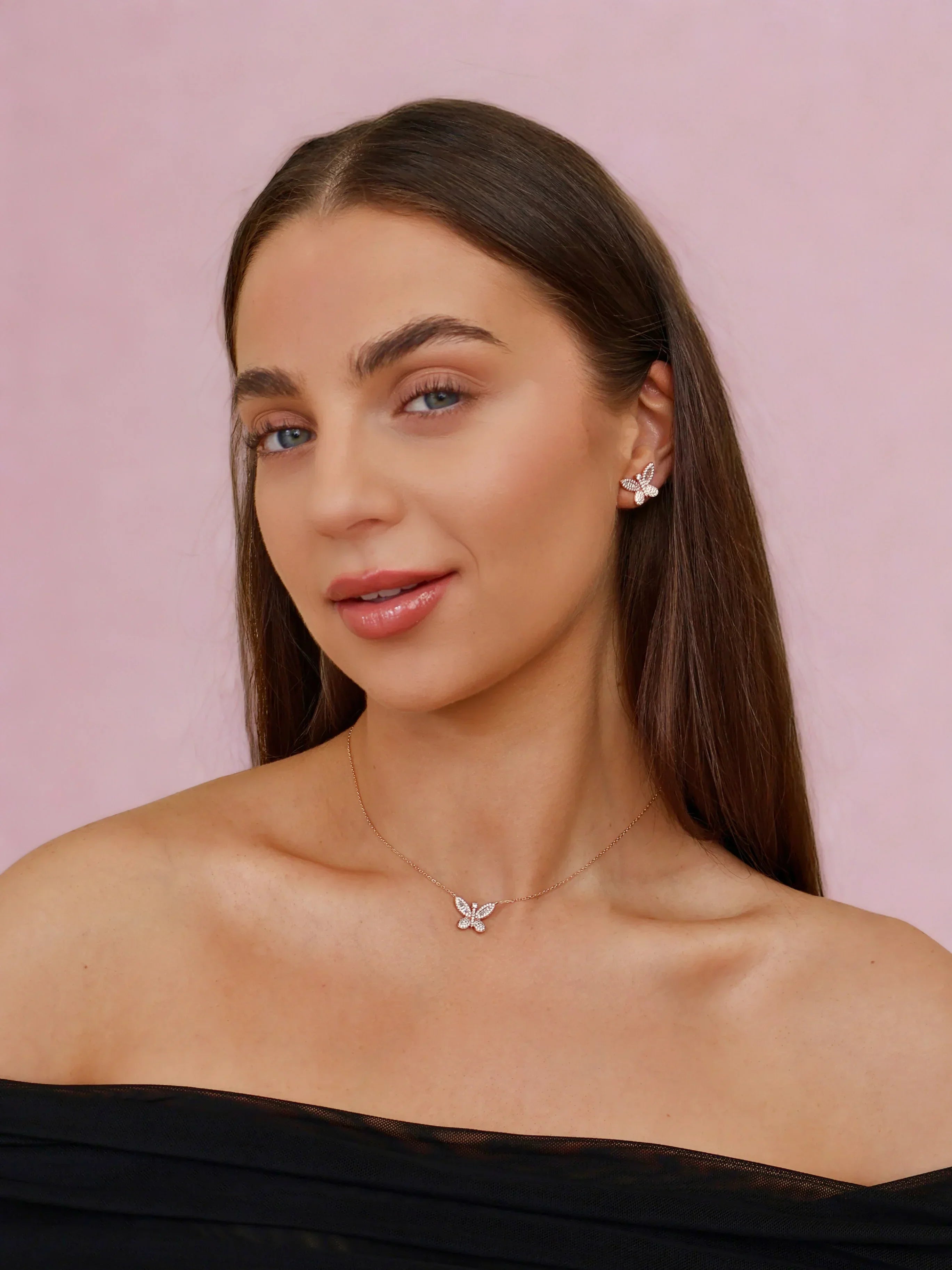 Woman wearing butterfly-shaped diamond earrings and matching necklace on pastel pink background