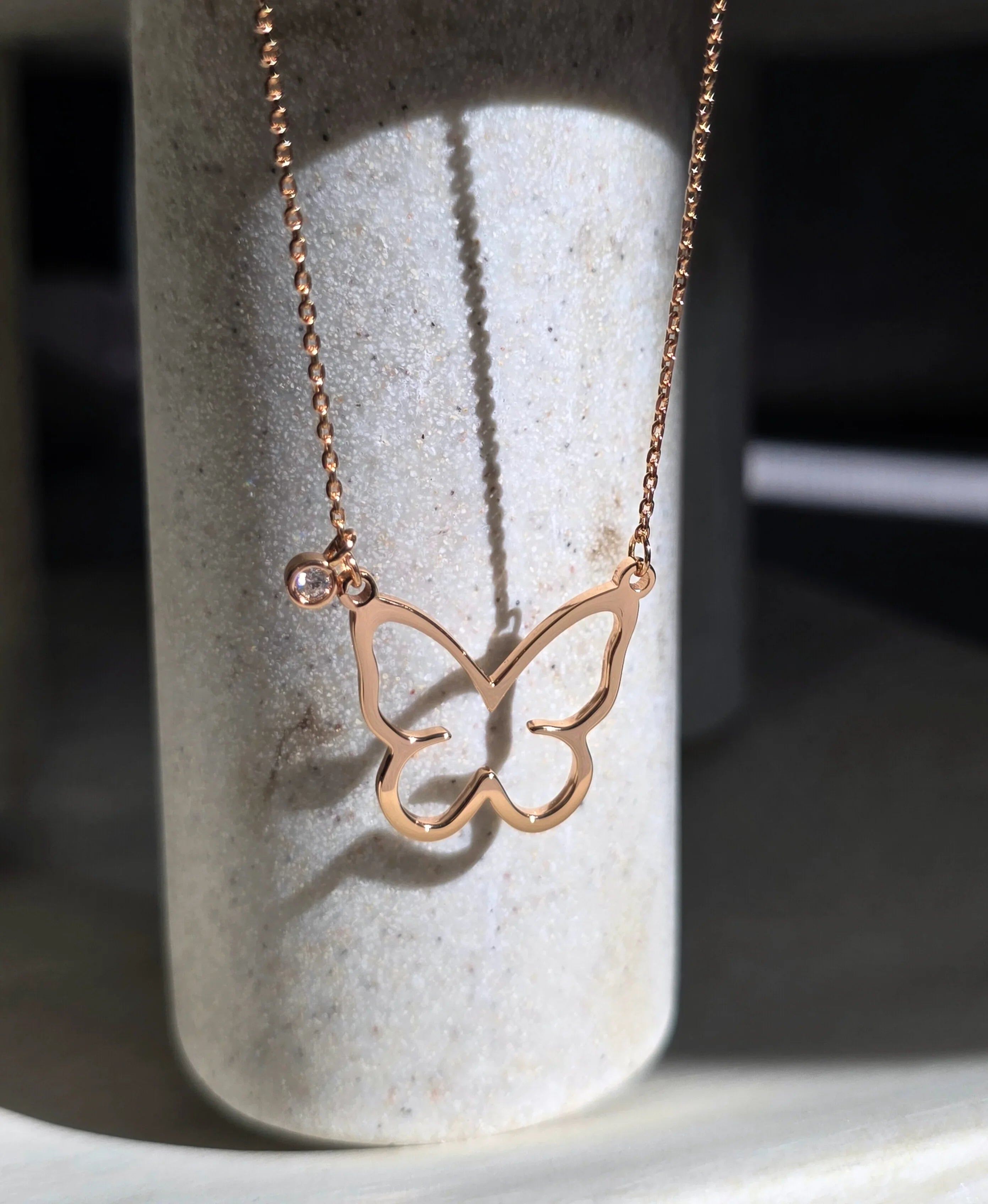 Rose gold butterfly necklace on a stone surface- front