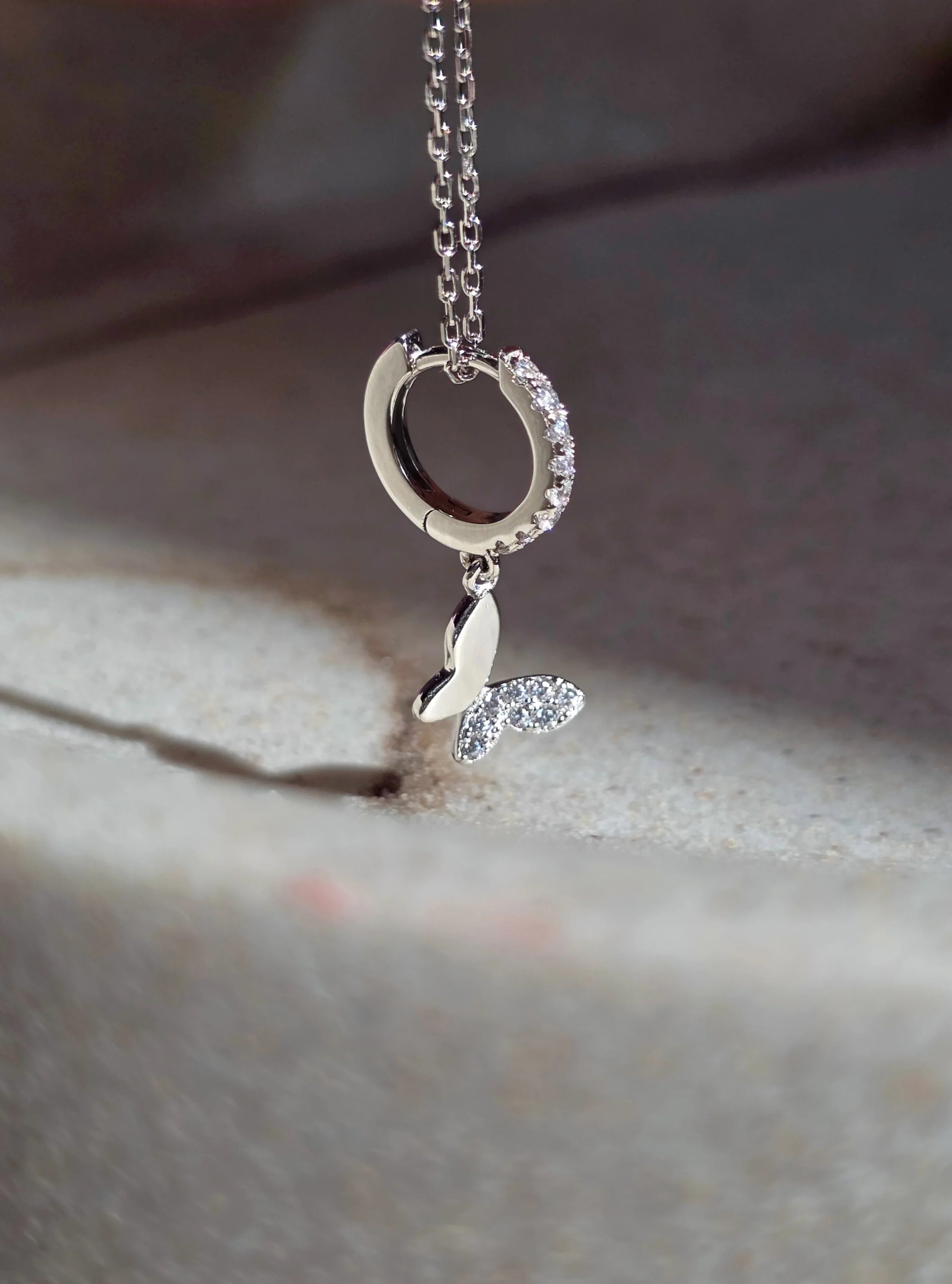 Silver huggie butterfly earrings with a heart-shaped pendant on a textured surface- close 