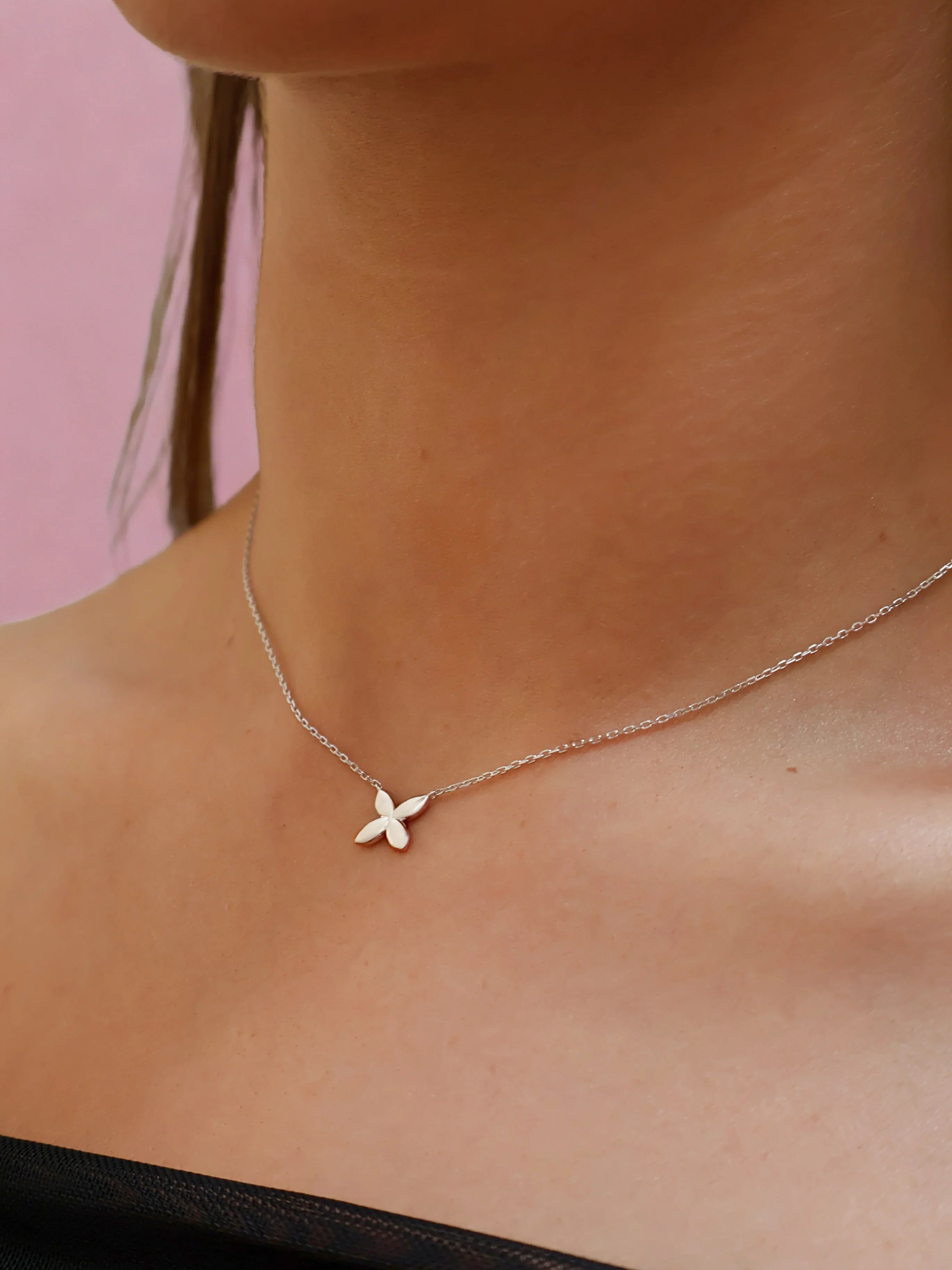 Delicate silver flower pendant necklace on a woman's neck with soft pink background
