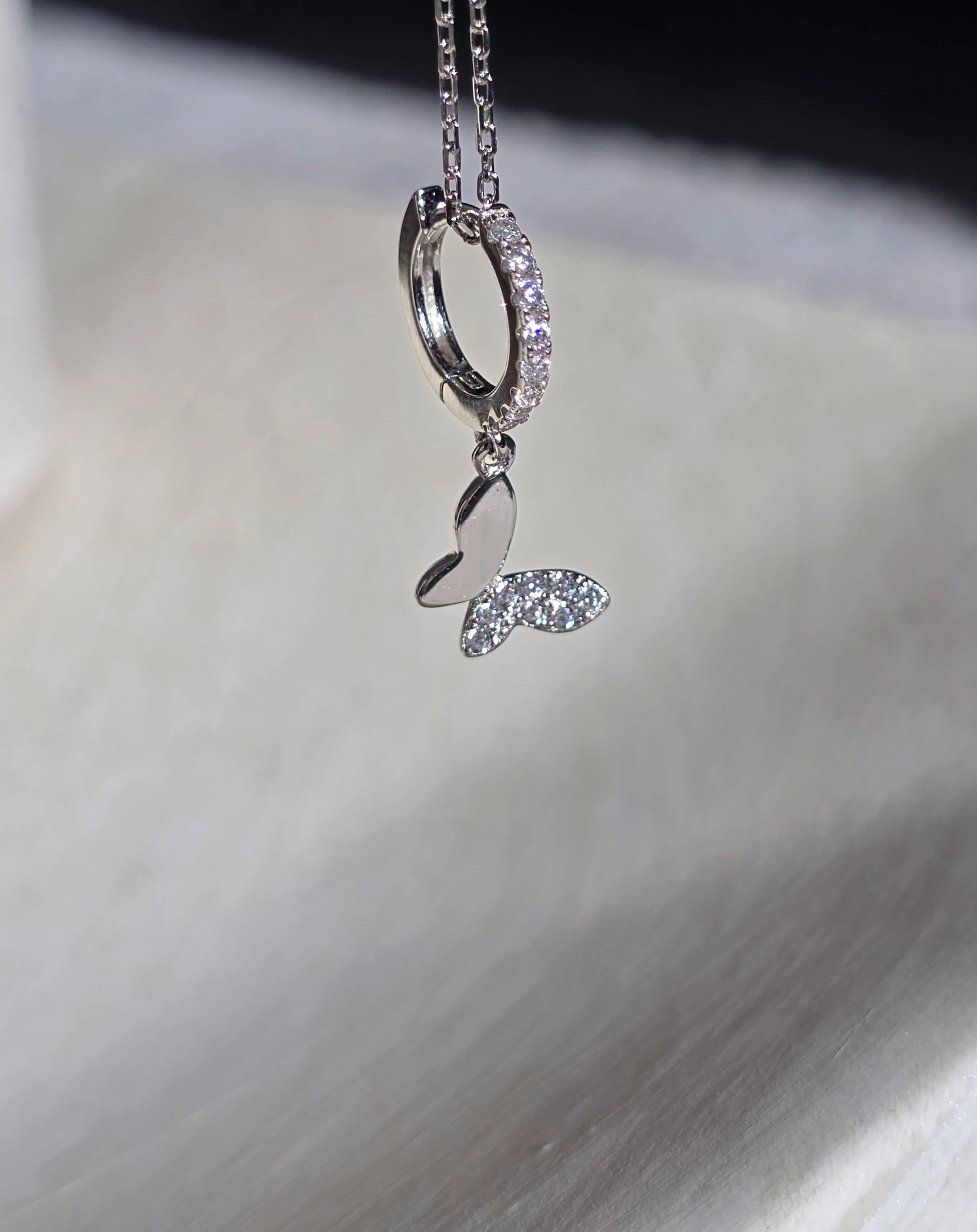 Silver huggie butterfly earrings with a heart-shaped pendant on a textured surface- close up 