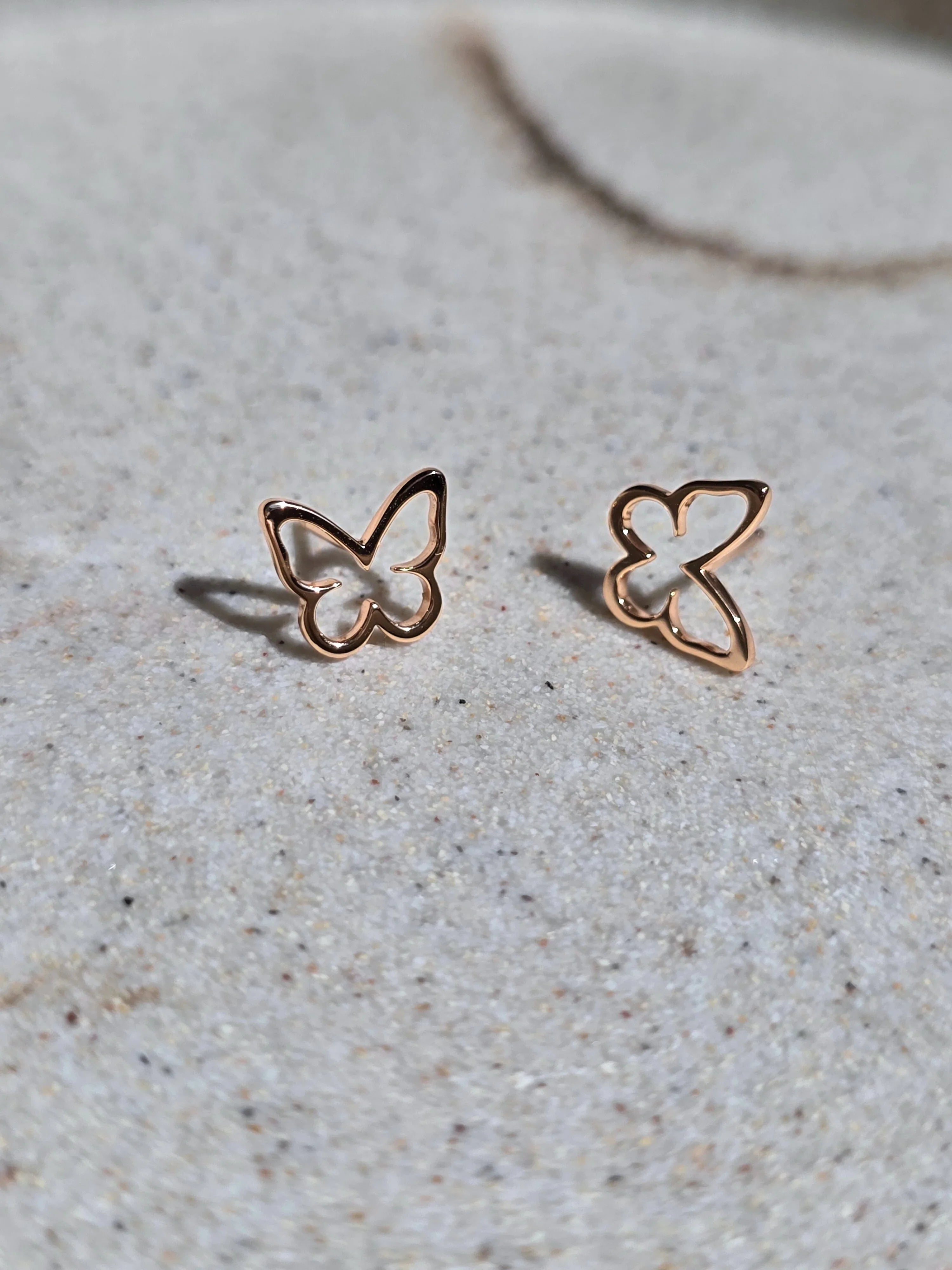 Rose gold butterfly-shaped earrings on a light gray surface- pair