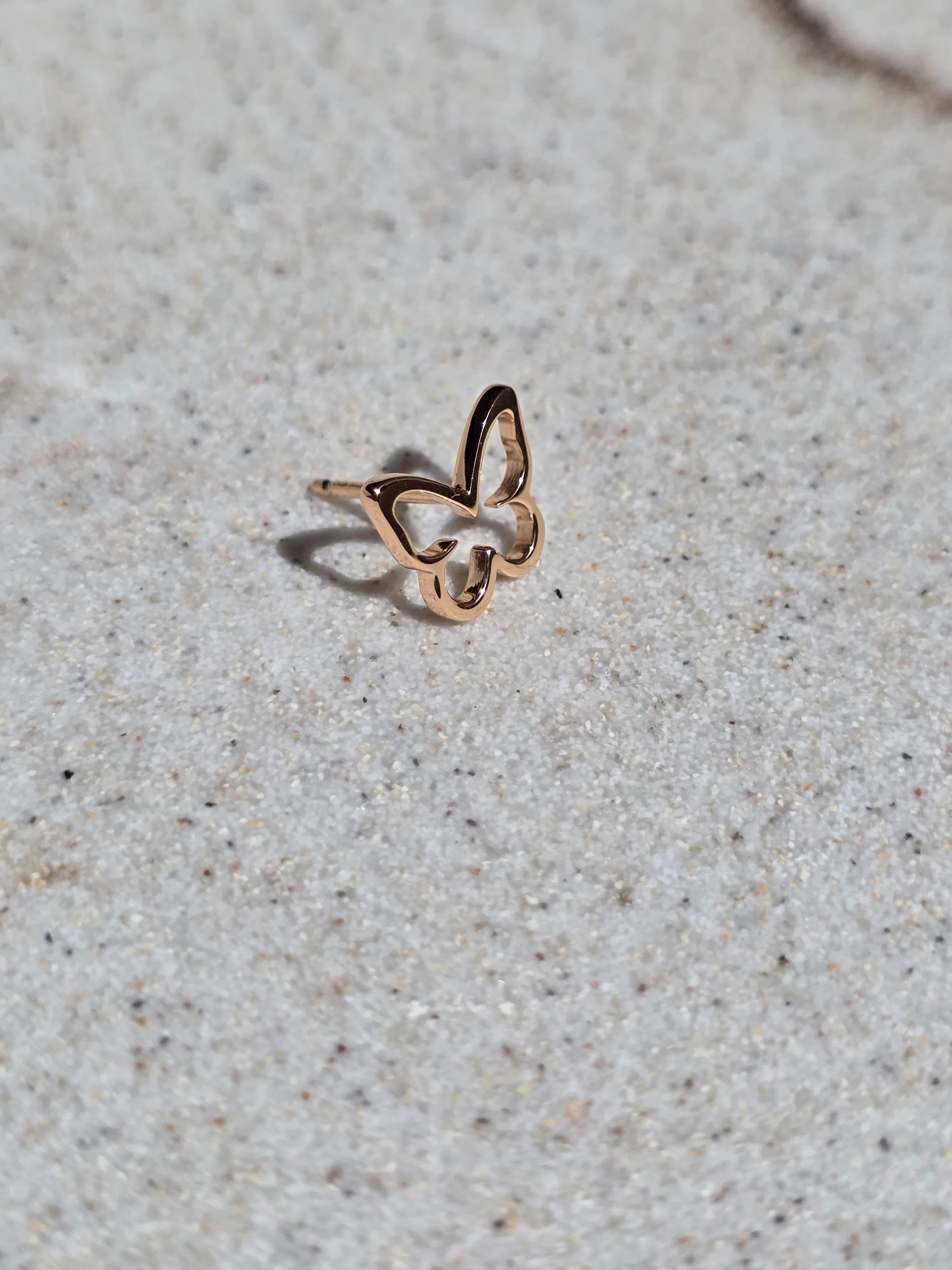 Rose gold butterfly-shaped ring on a light gray surface- front