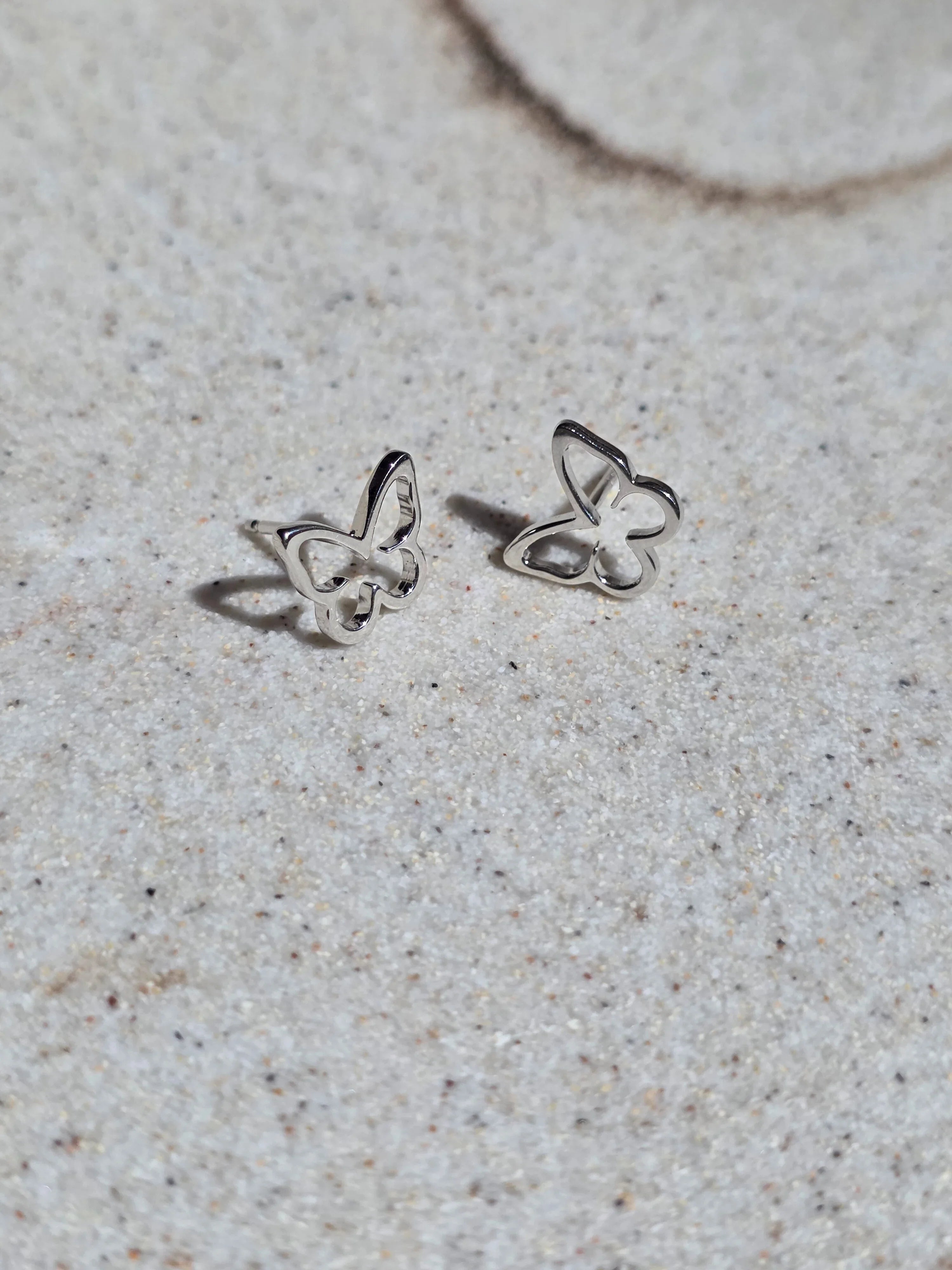 Silver butterfly earrings on a sandy surface- pair