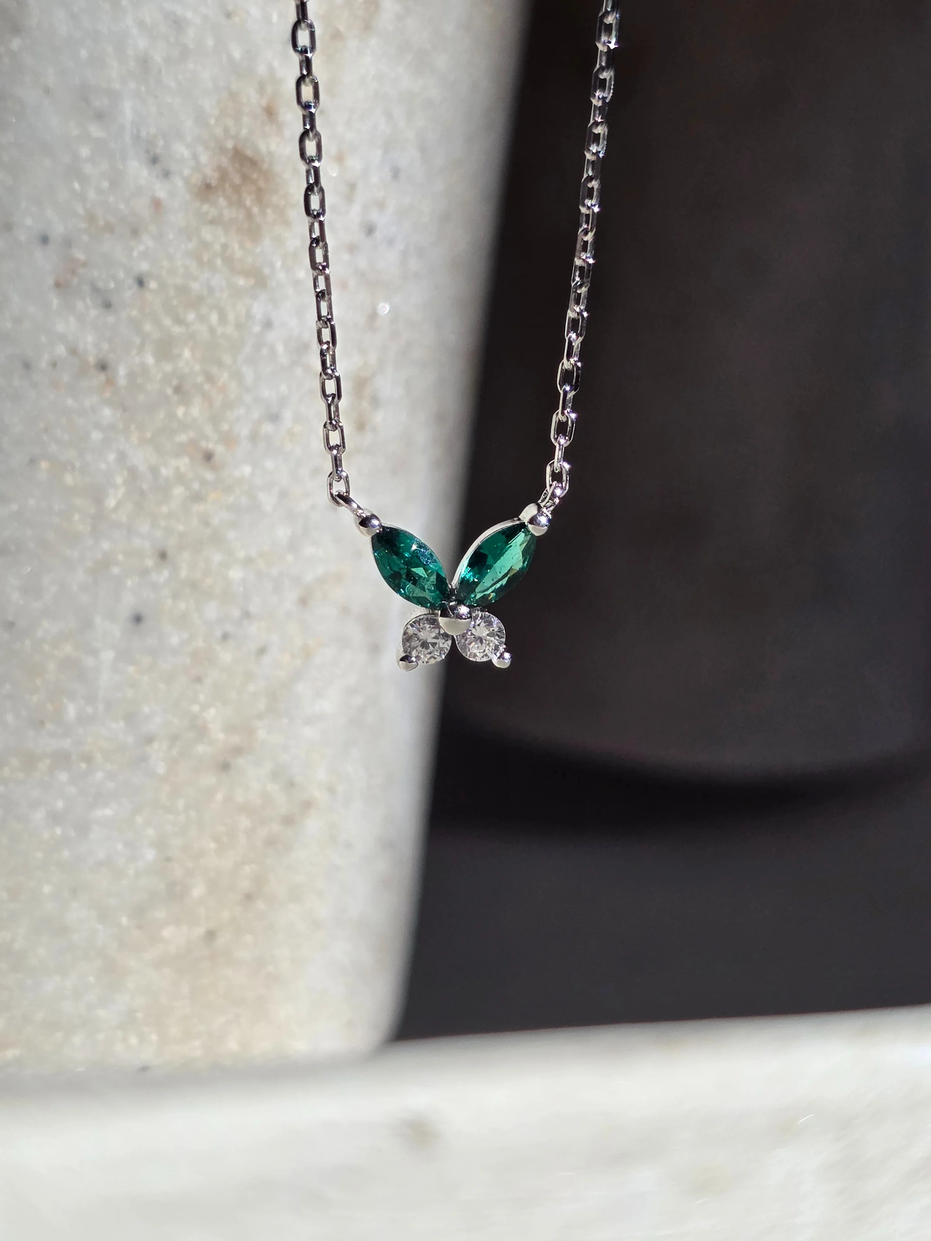 Petite Butterfly Necklace silver with butterfly pendant featuring green gemstones on a textured surface