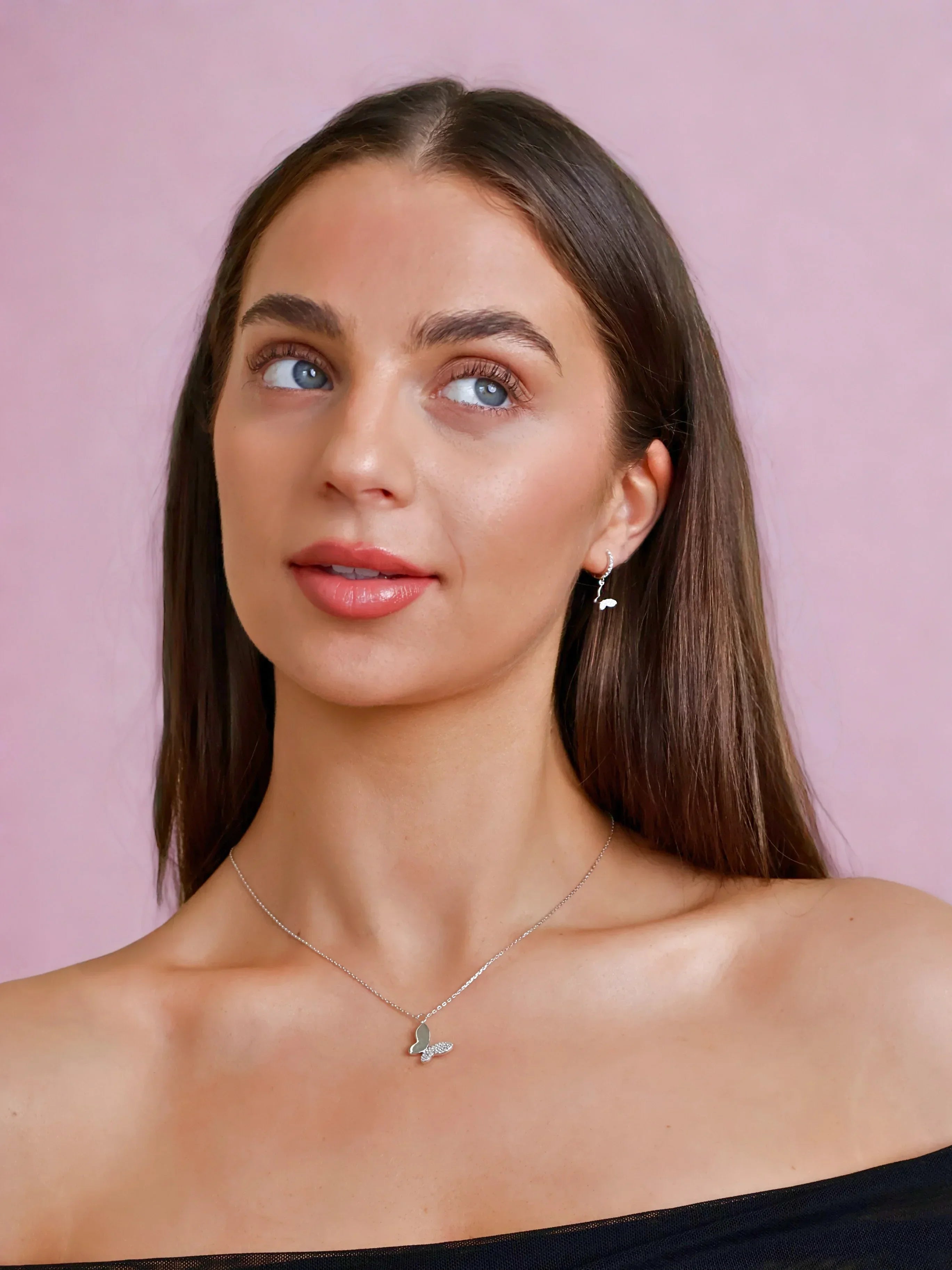 Woman wearing silver butterfly necklace and matching earrings against pink background, Marwa Jewels