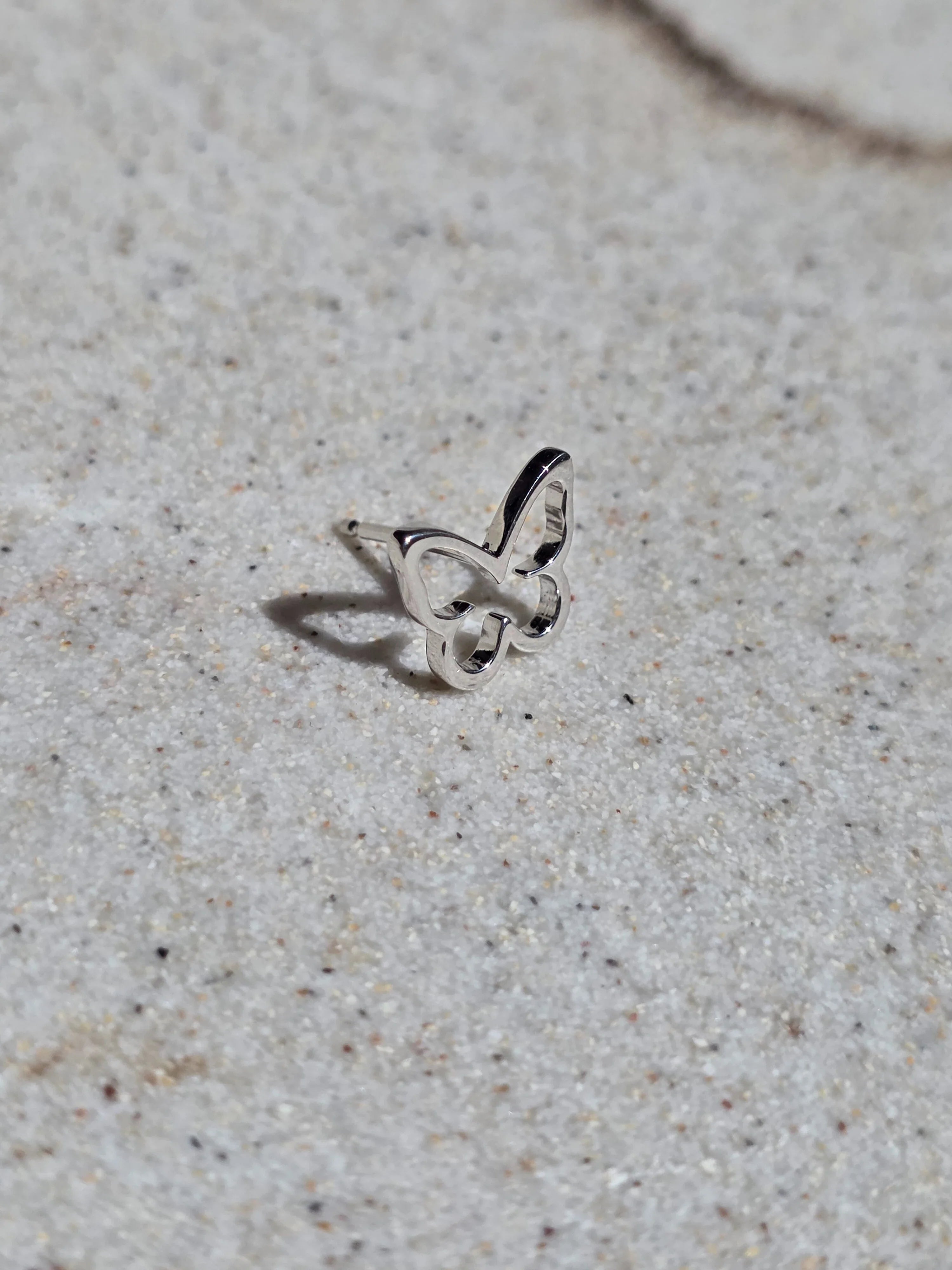 Butterfly-shaped silver earring on a textured beige surface- side