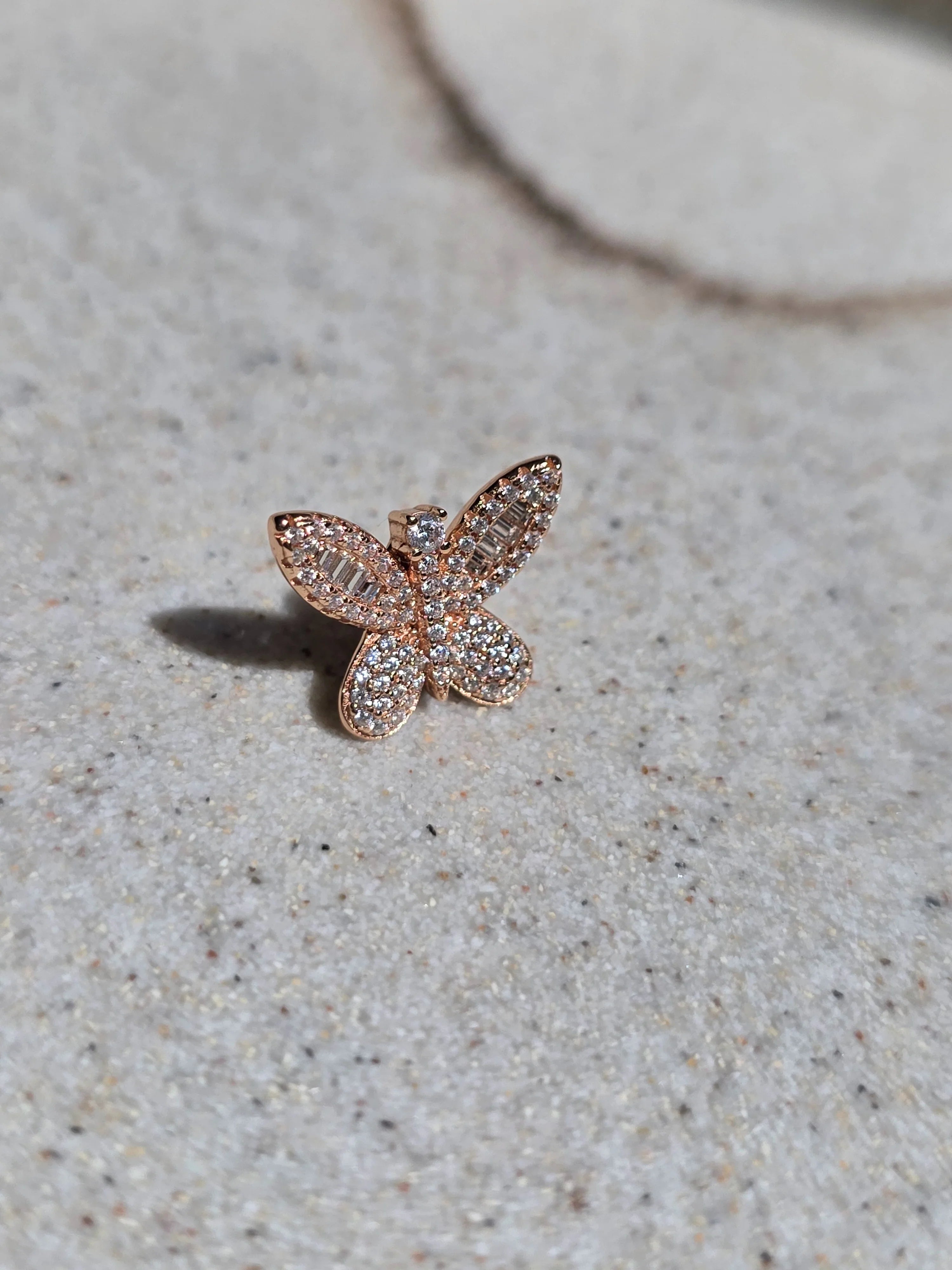 Rose gold butterfly-shaped earring on a textured beige surface - side