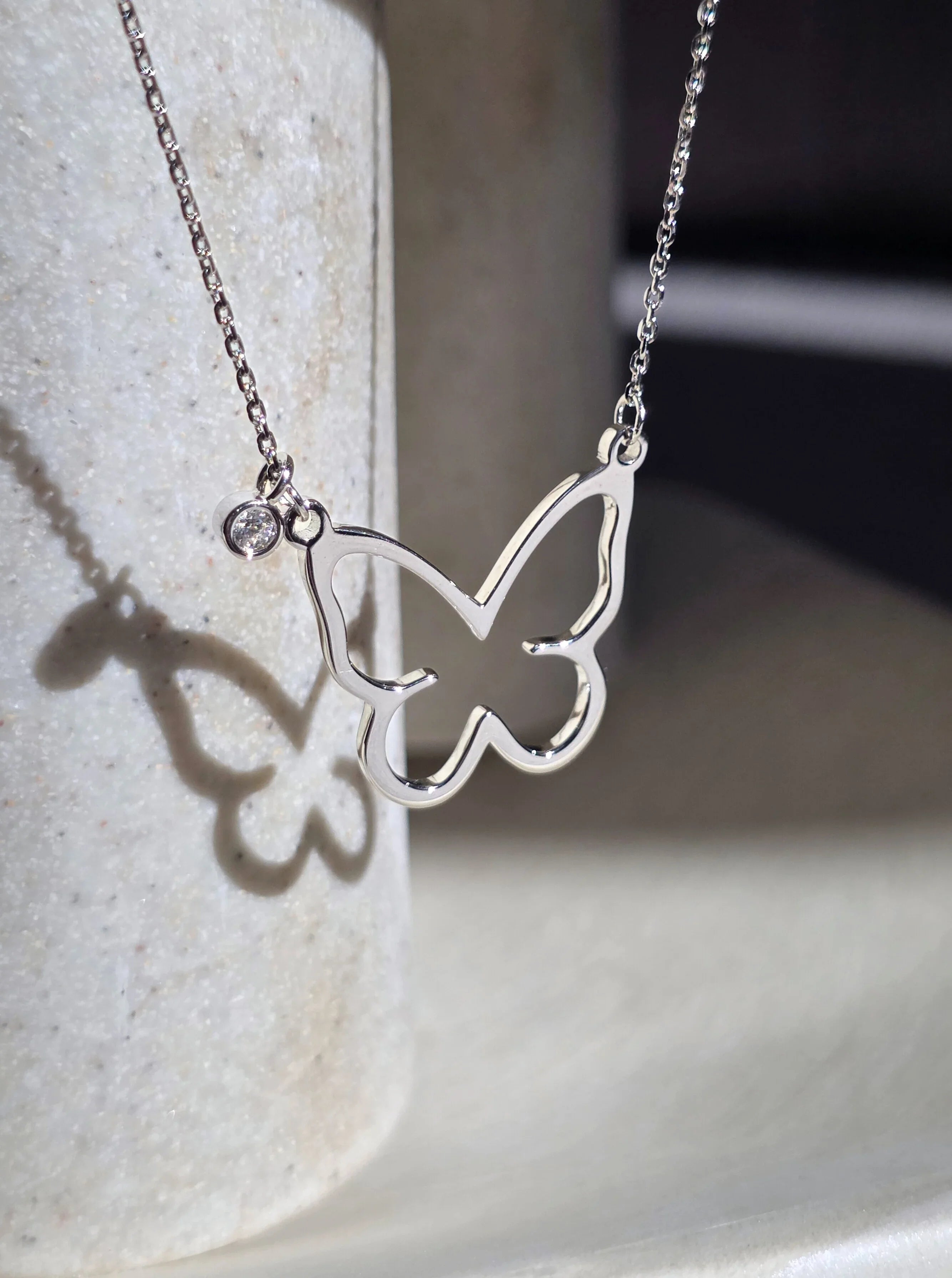 Silver butterfly necklace on a light stone surface- sode ways