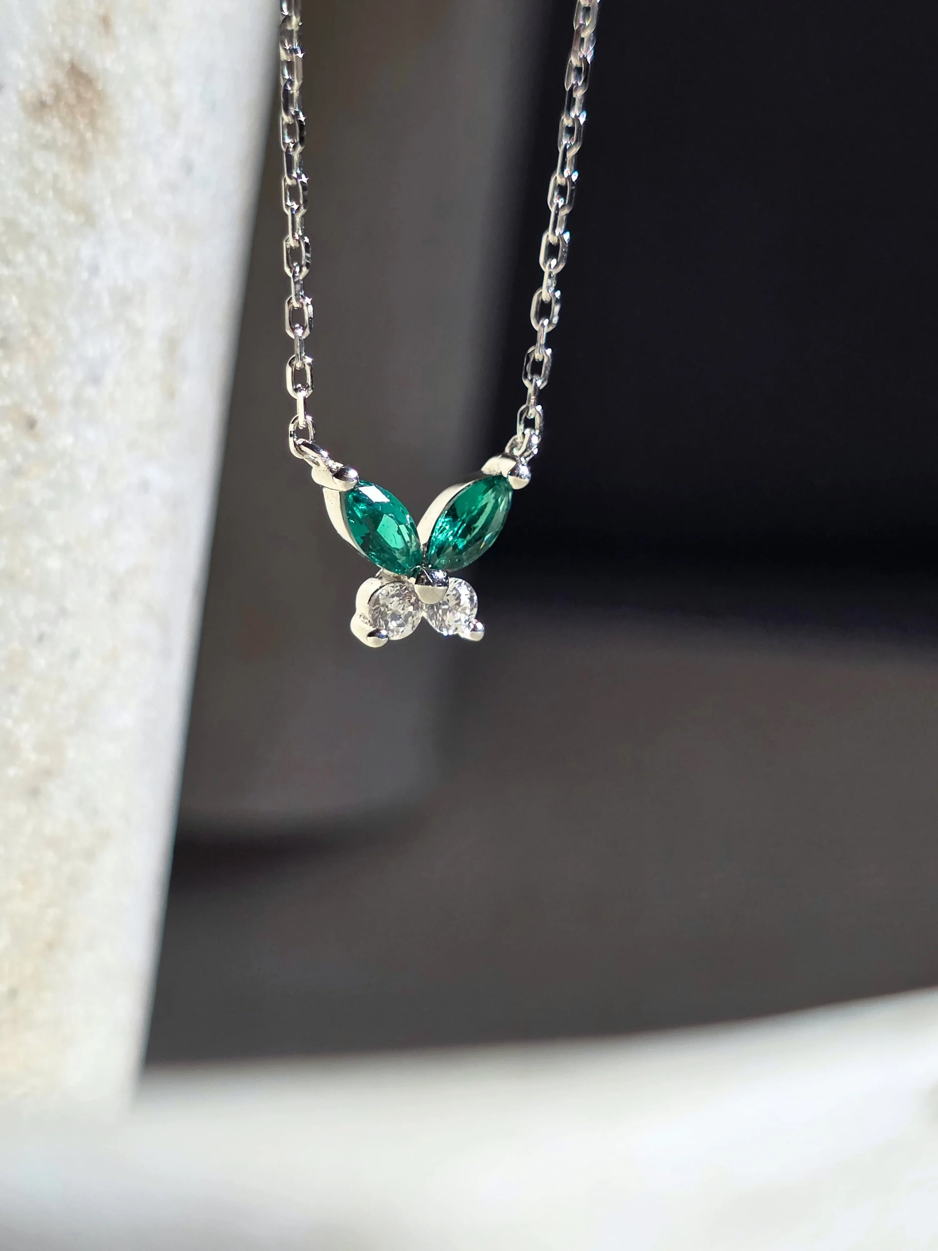 Petite Butterfly Necklace silver with butterfly pendant featuring green gemstones on a textured surface side ways