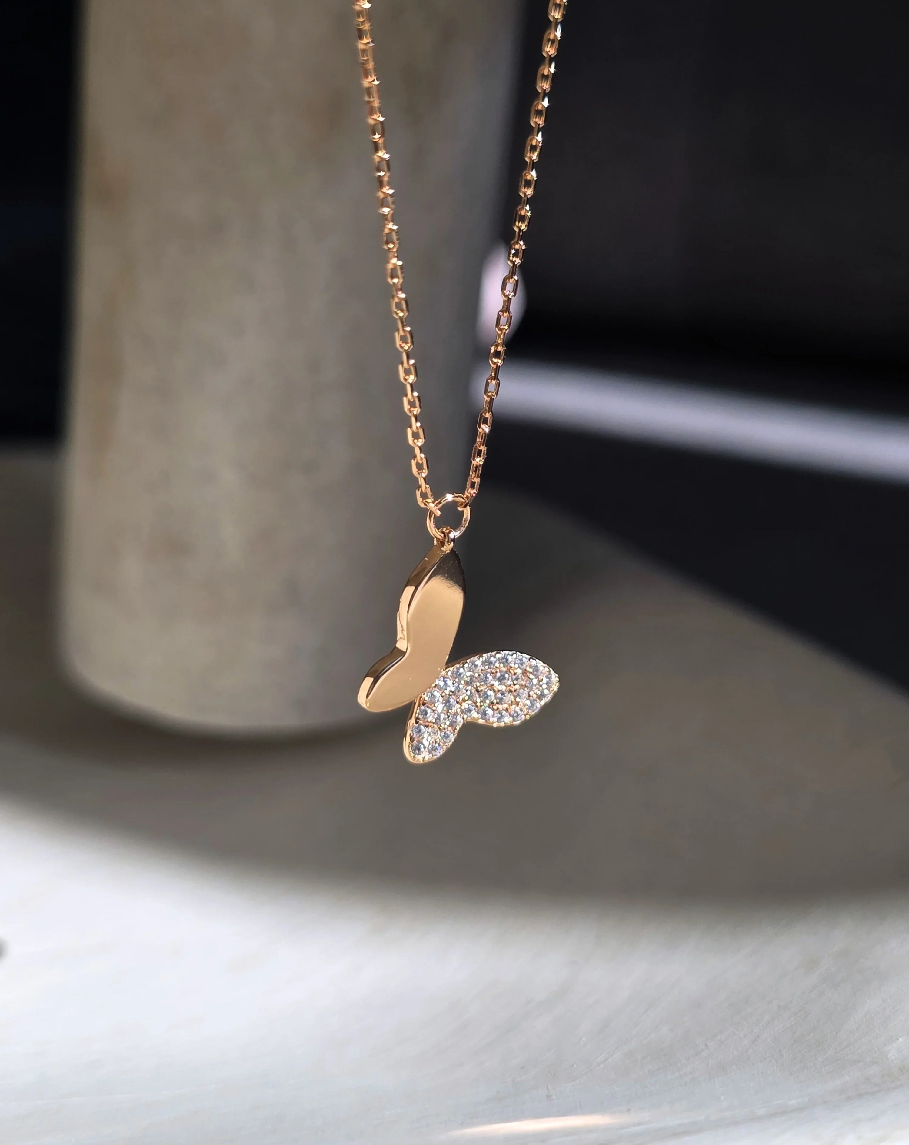 Gold necklace with a butterfly pendant on a neutral background- side ways- further a bit