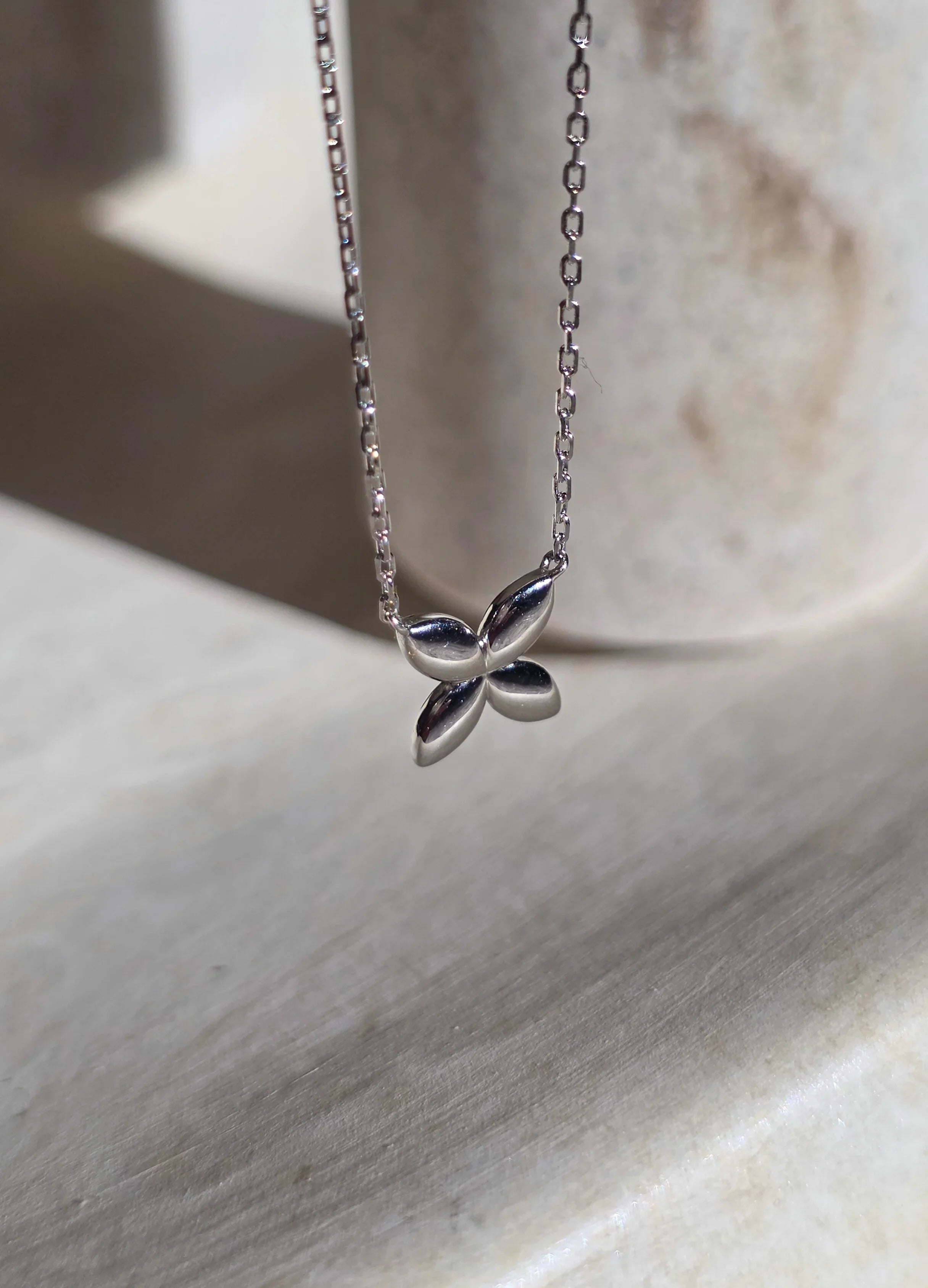 Silver butterfly necklace on a marble surface- side ways