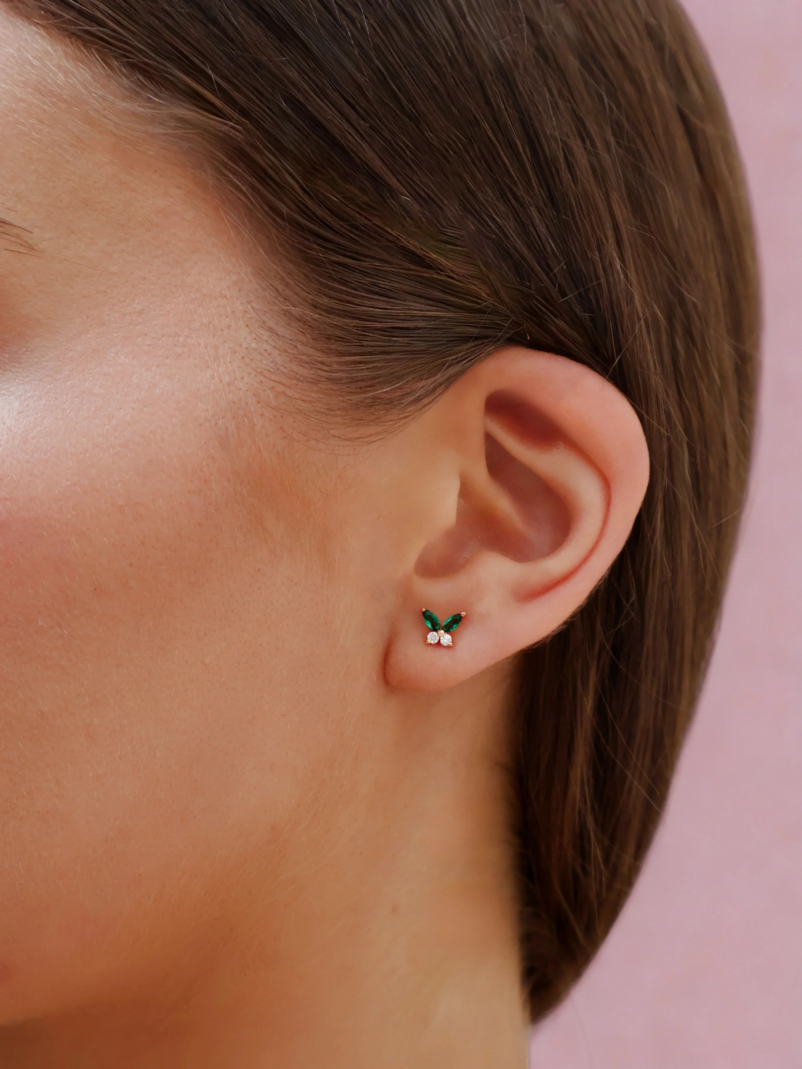 Close-up of an ear wearing a small earring with a pink background