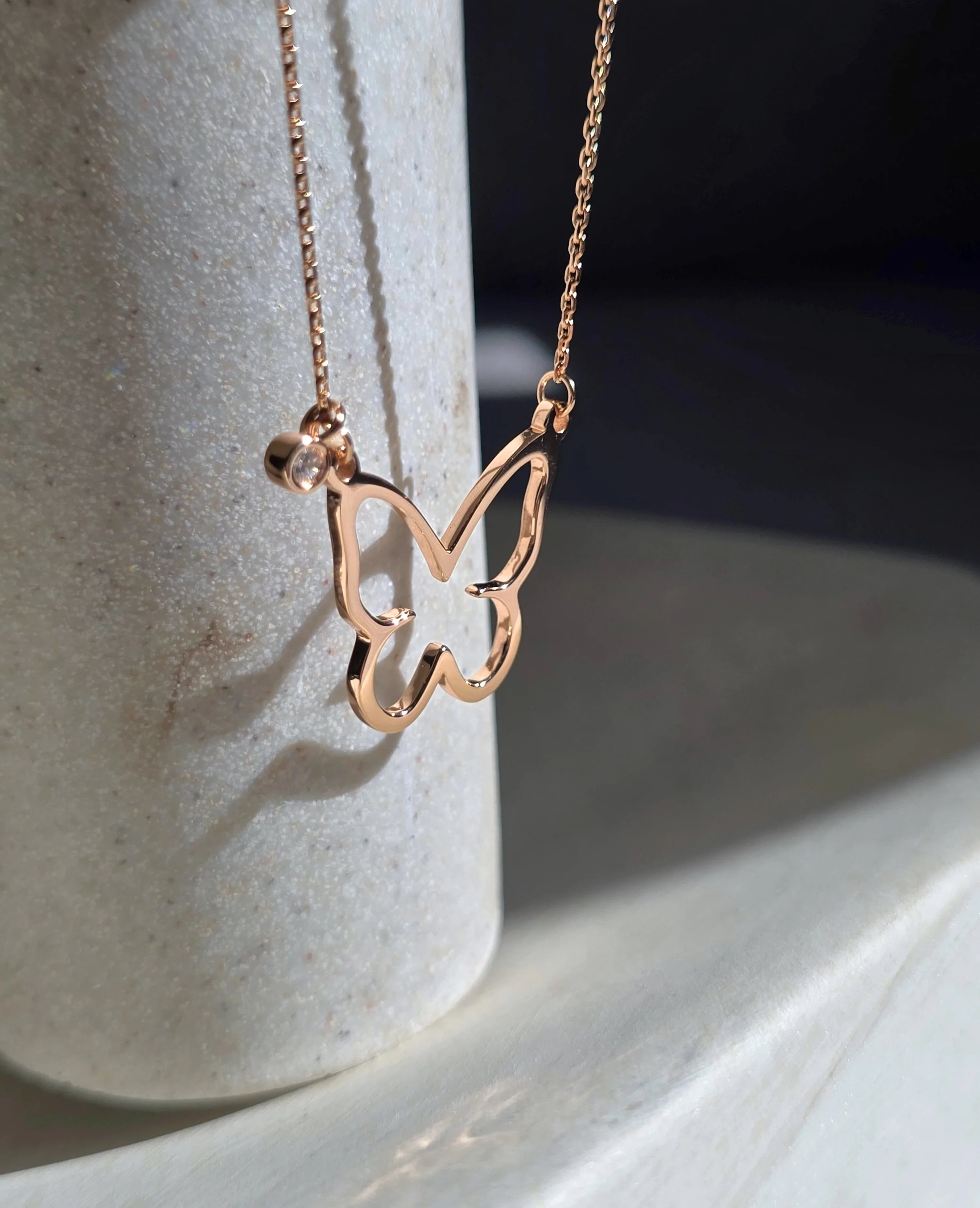 Rose gold butterfly necklace on a light stone surface- side ways