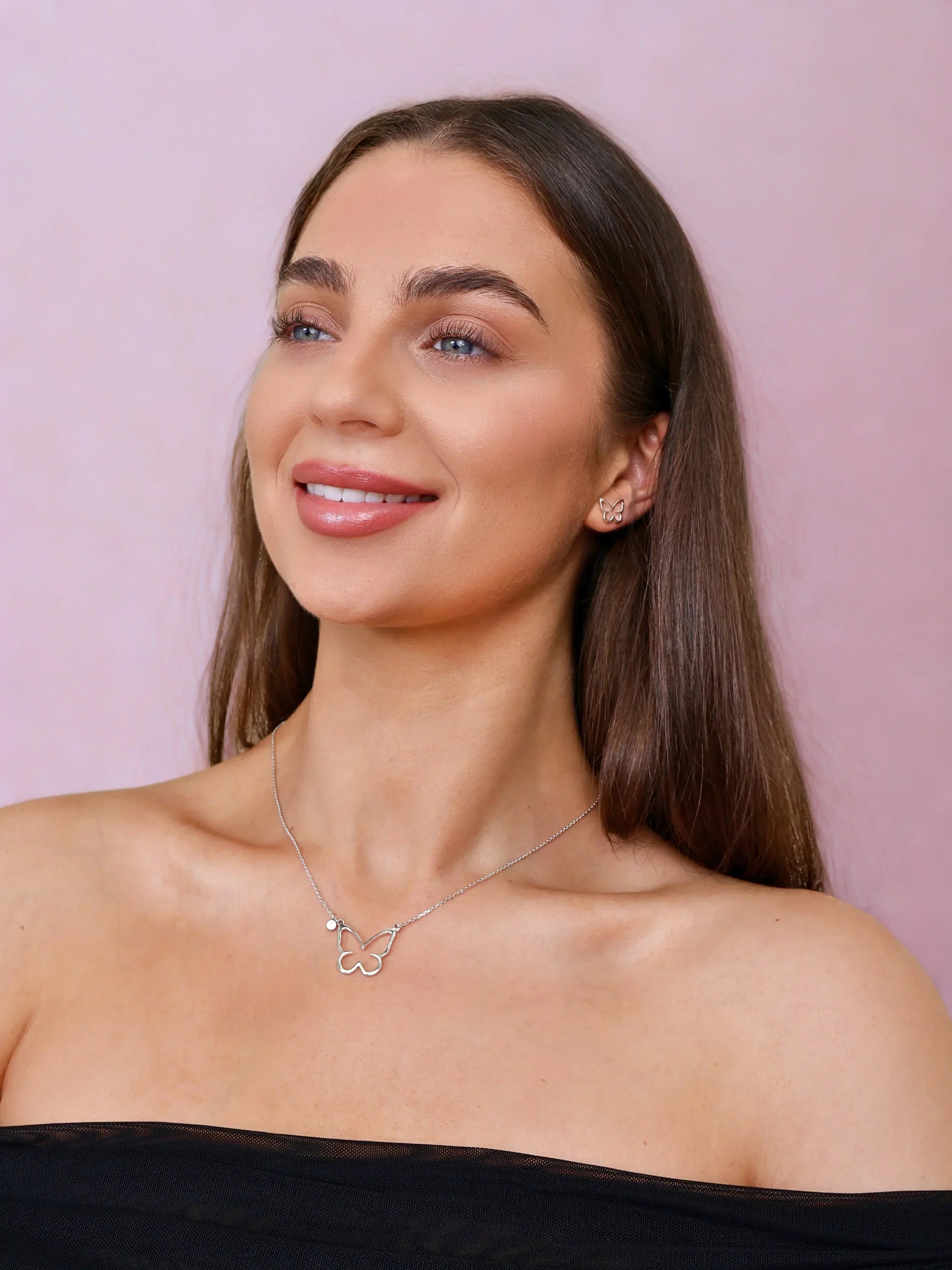 Woman wearing silver butterfly necklace and matching earrings with pink background