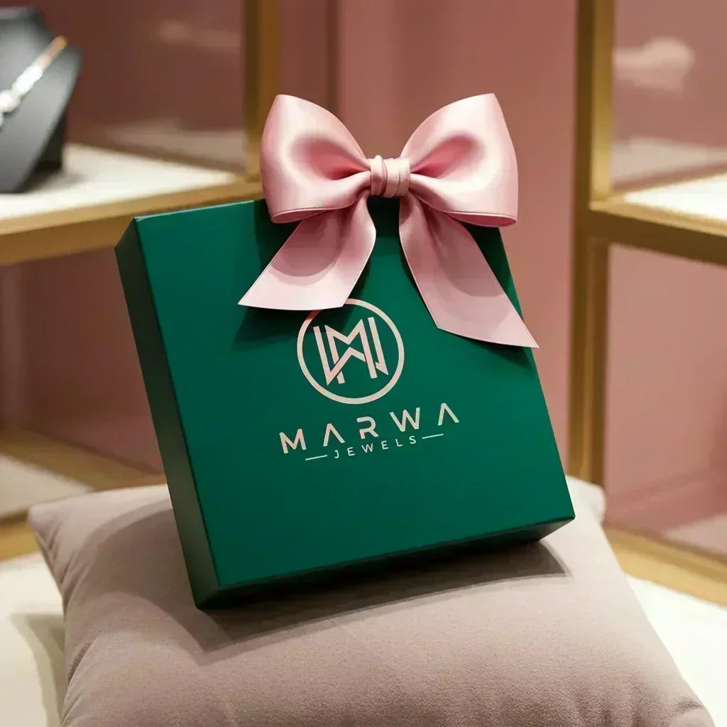 Green Marwa Jewels gift box with pink satin bow displayed on beige cushion in store