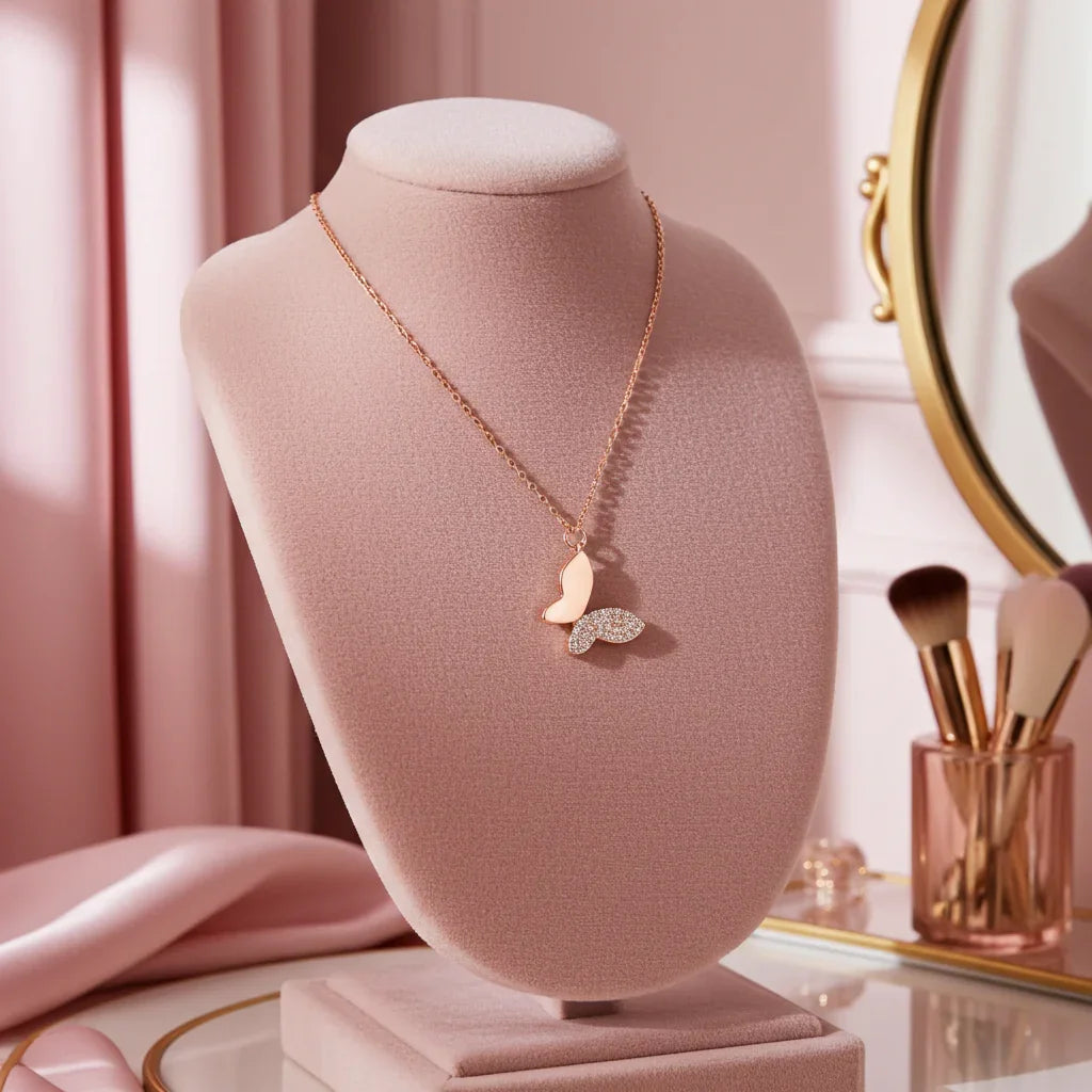 Rose gold butterfly necklace with sparkling wings displayed on a pink velvet stand with makeup brushes and a mirror nearby