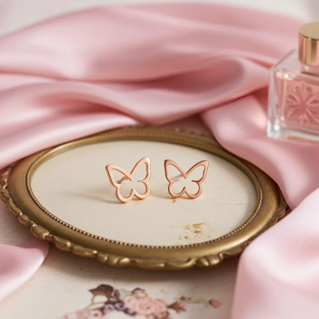 Rose gold butterfly-shaped earrings on vintage gold-trimmed mirror tray with pink satin fabric