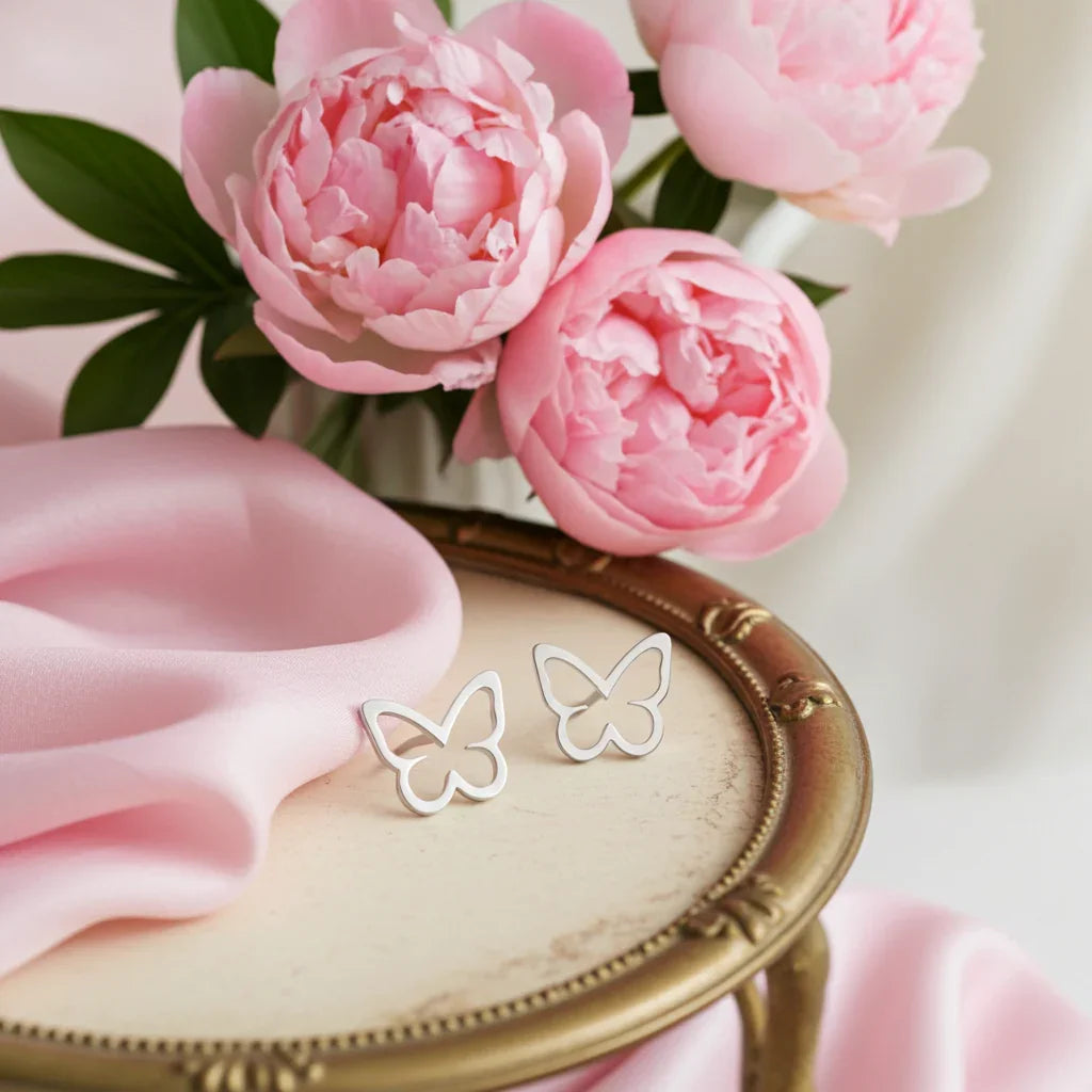 Silver open butterfly earrings on vintage round table with pink peonies and soft pink fabric