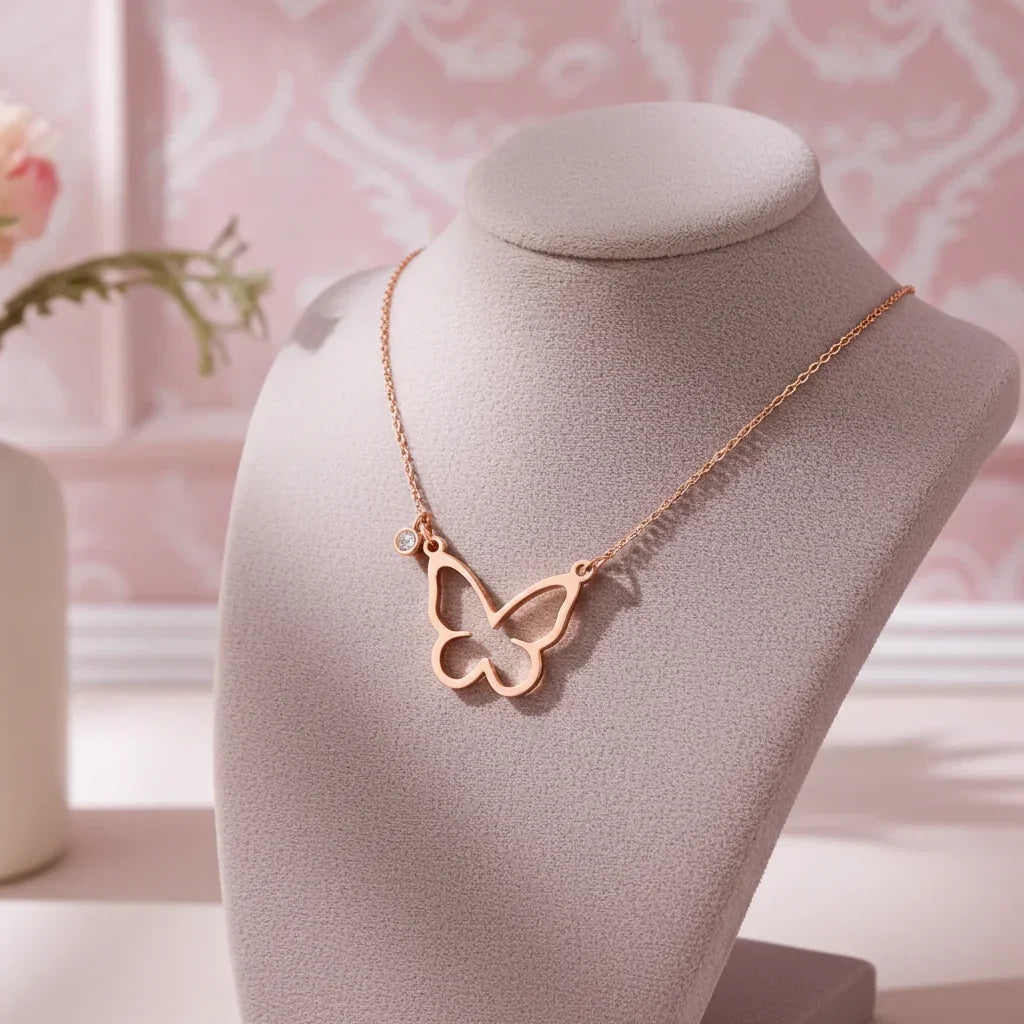 Rose gold open butterfly necklace with small crystal charm displayed on a beige necklace stand