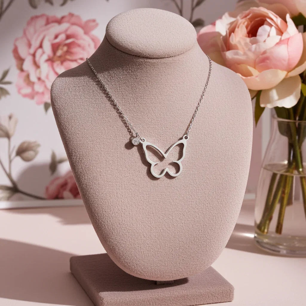 Silver open butterfly necklace displayed on pink bust with floral backdrop and pink roses in glass vase