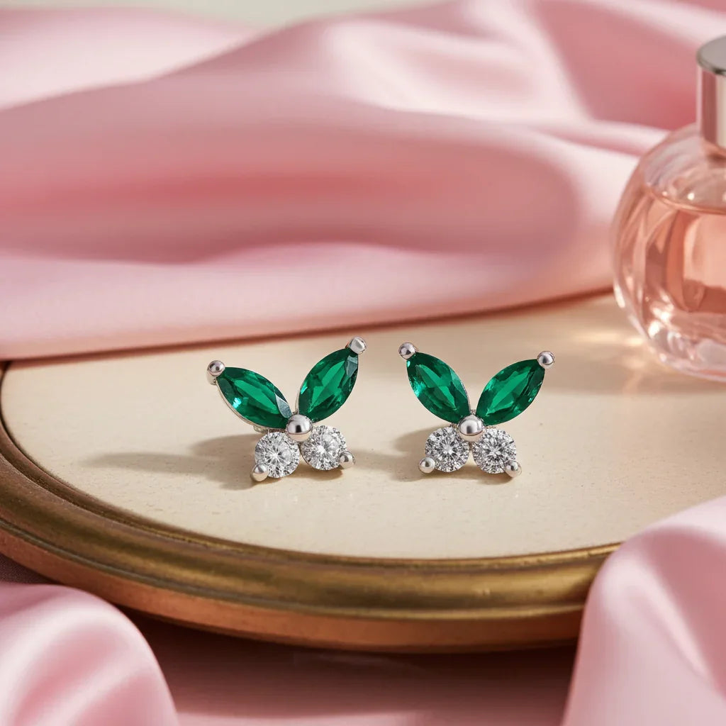 Green gemstone earrings on a pink fabric background with a perfume bottle.