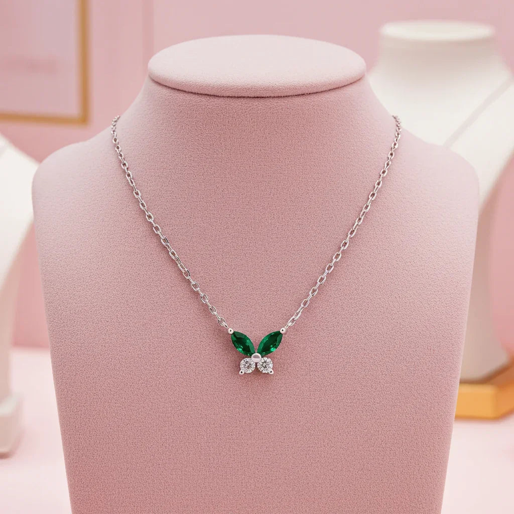 Silver butterfly necklace with green and clear stones displayed on pink velvet bust