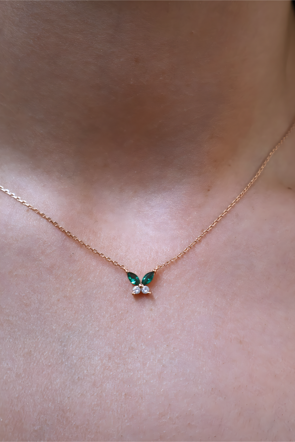 Butterfly-shaped necklace with green gemstones on a person's neck