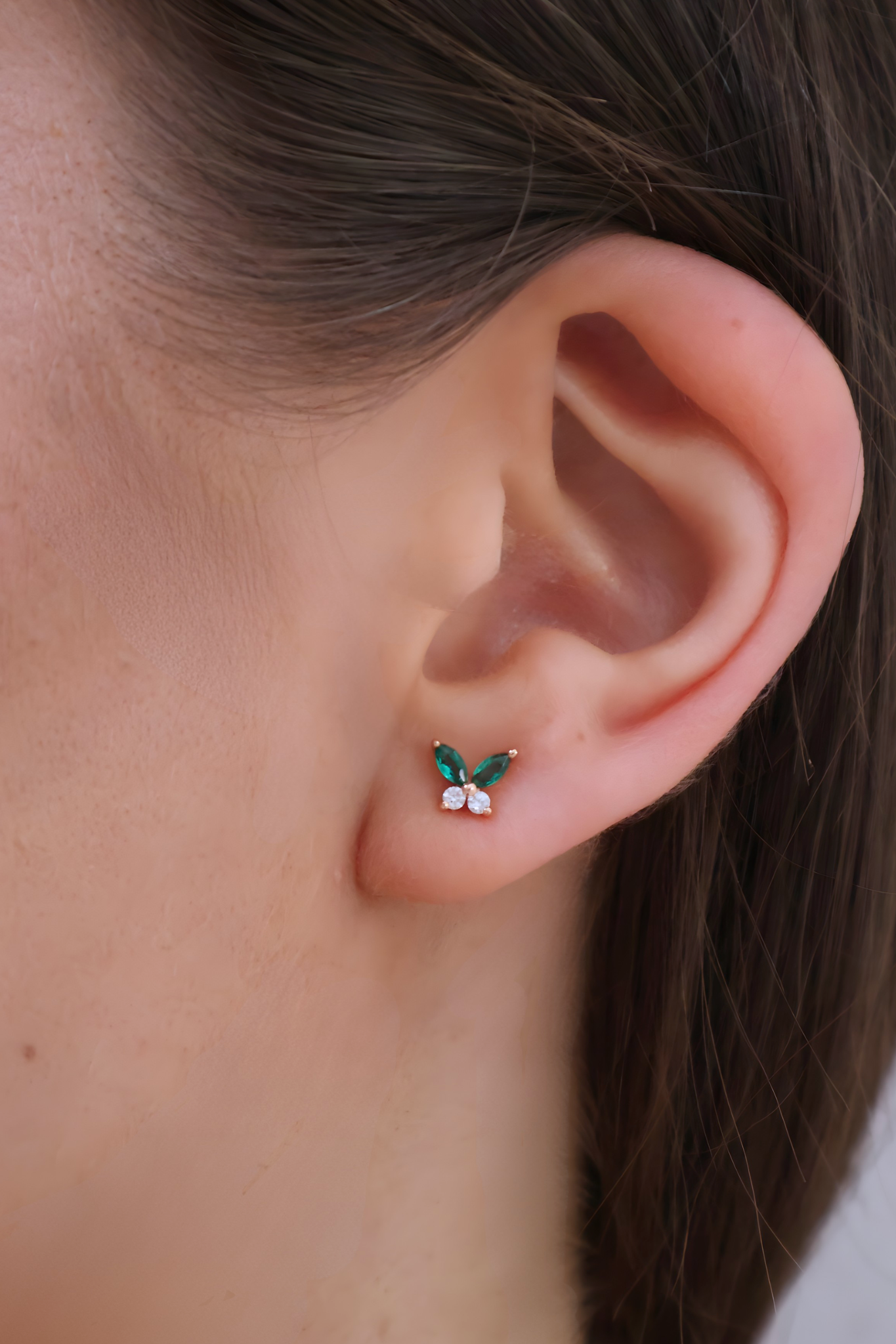 Close-up of an ear wearing a small earring with green gemstones.