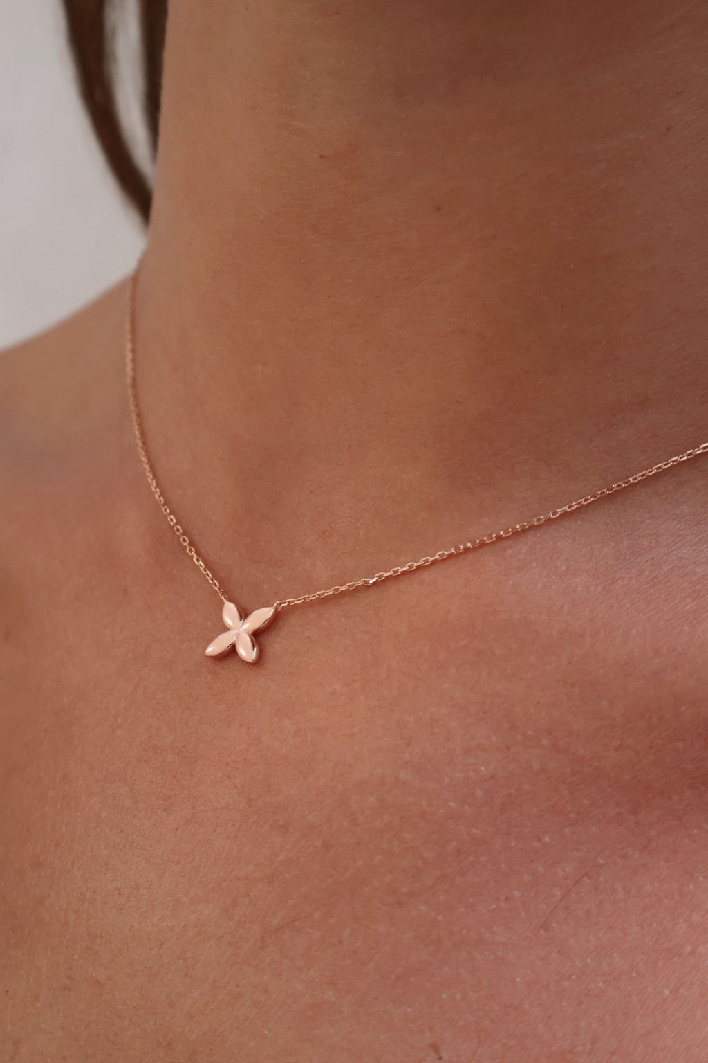 Rose gold necklace with a small pendant on a person's neck against a neutral background