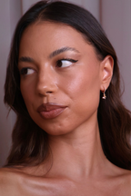 Woman with a neutral expression wearing a gold earring against a plain background
