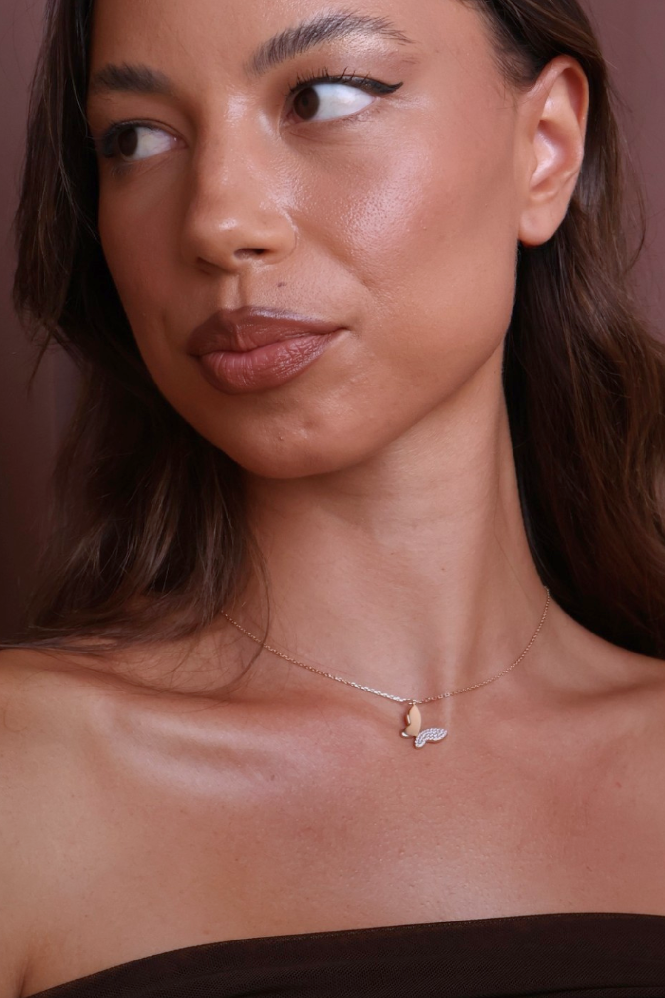Close-up of a woman wearing a delicate necklace against a brown background
