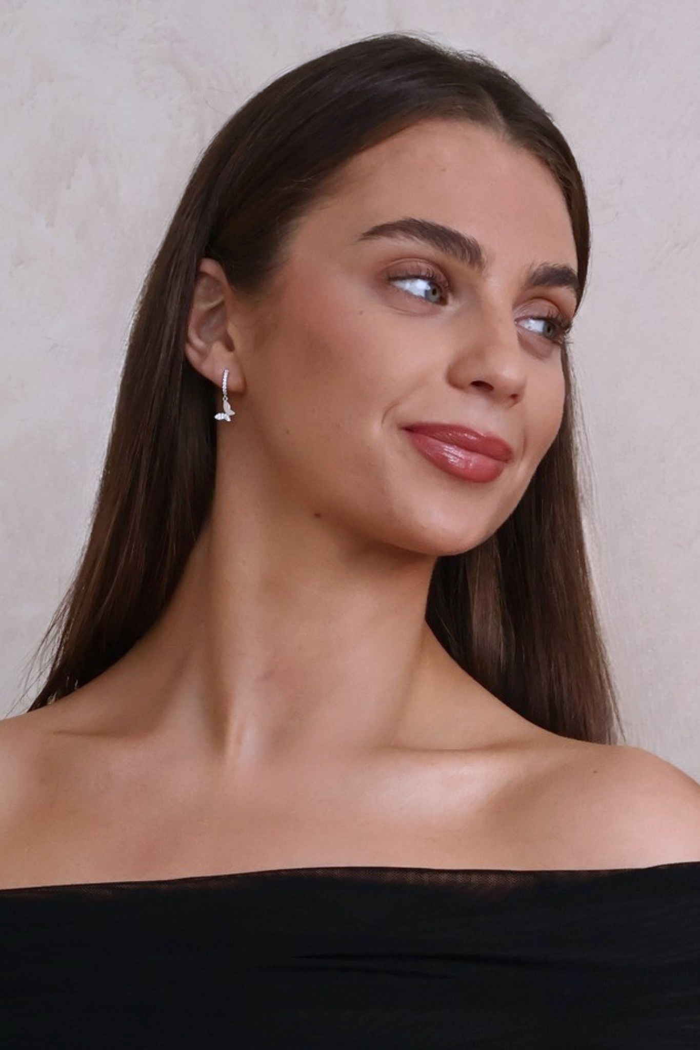 Woman with long brown hair wearing a black off-shoulder top against a neutral background