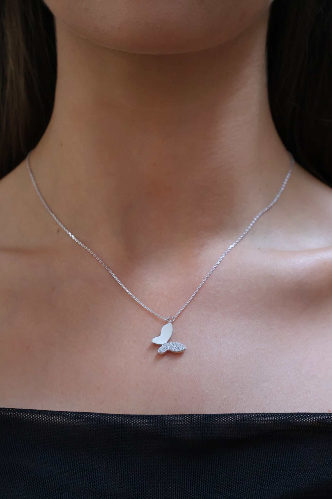 Silver butterfly necklace on a person's neck against a dark background