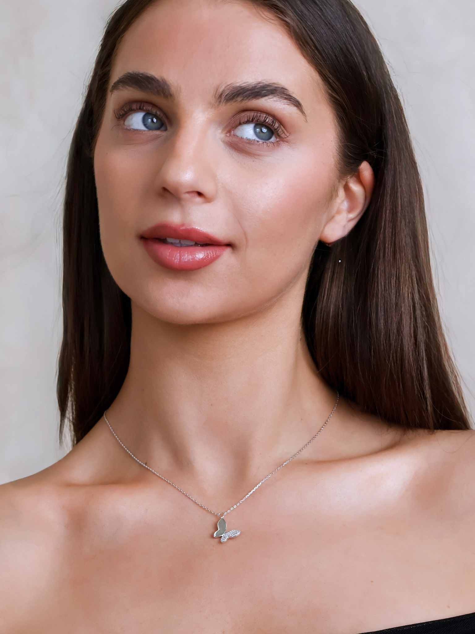 Woman wearing a silver necklace with a butterfly pendant against a neutral background