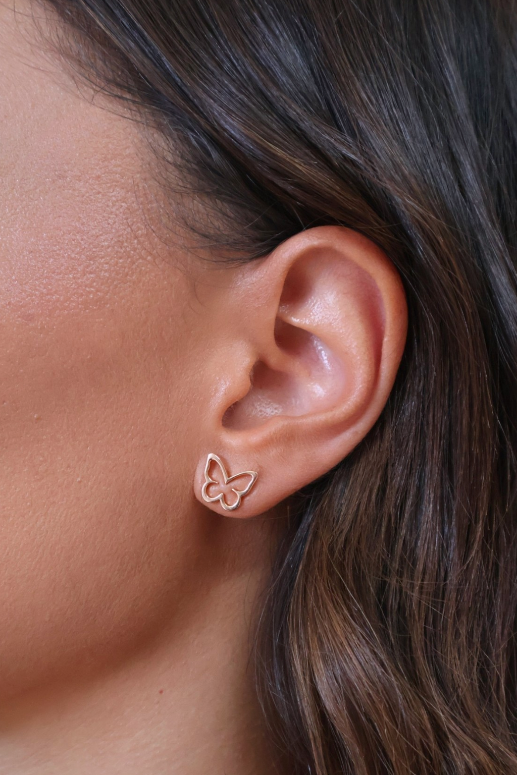 Close-up of an ear wearing a butterfly-shaped earring with a blurred background