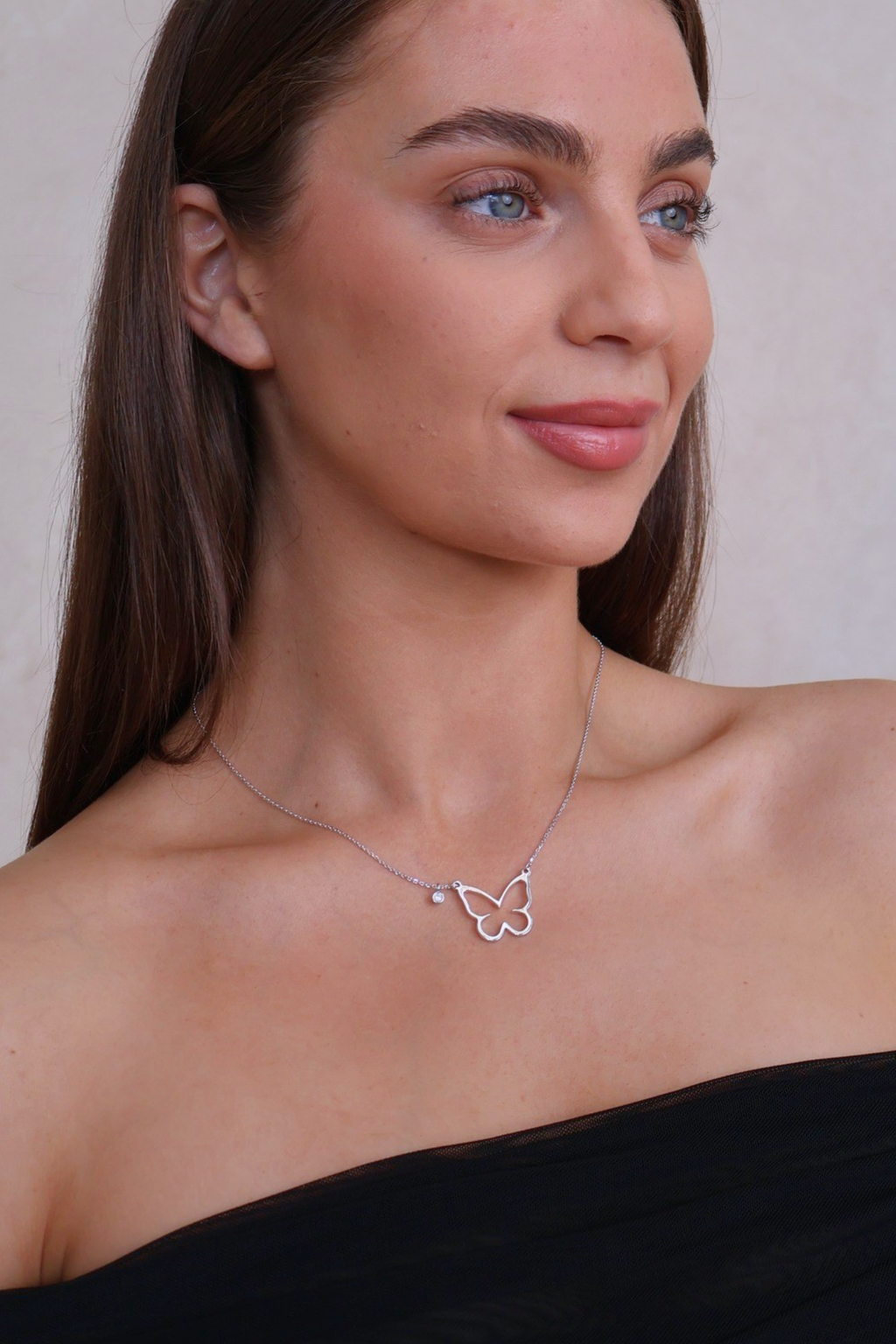 Woman wearing a butterfly necklace against a neutral background