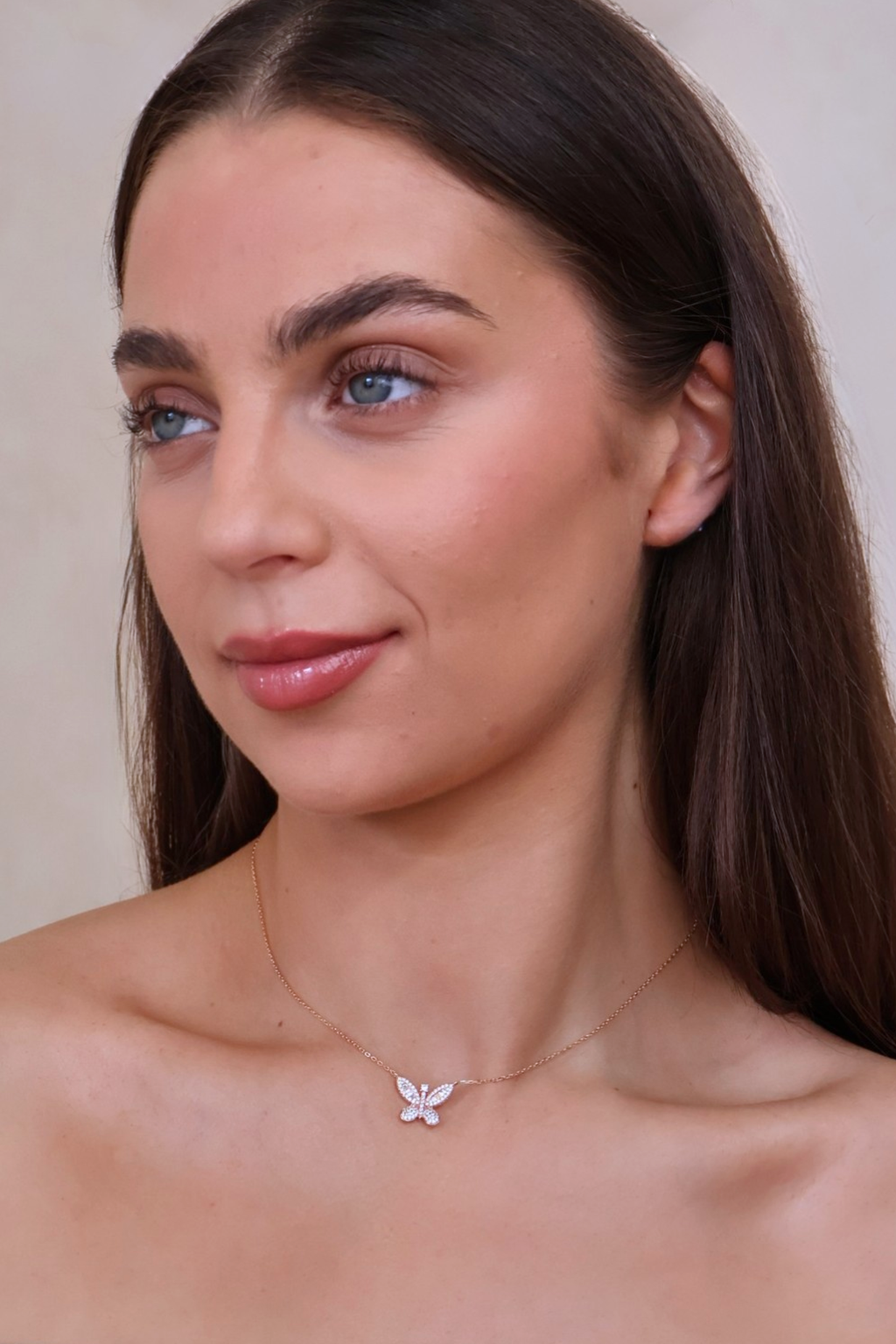 Woman wearing a delicate necklace with a butterfly pendant against a neutral background