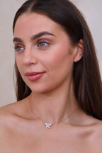 Woman wearing a delicate necklace with a butterfly pendant against a neutral background