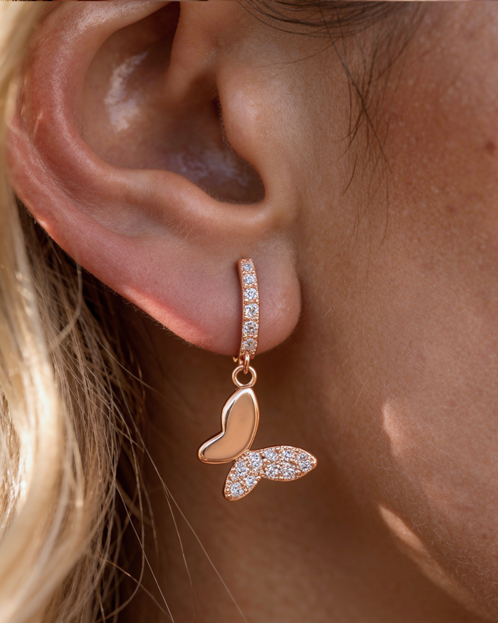 Rose gold butterfly earring with clear stones worn by a person.