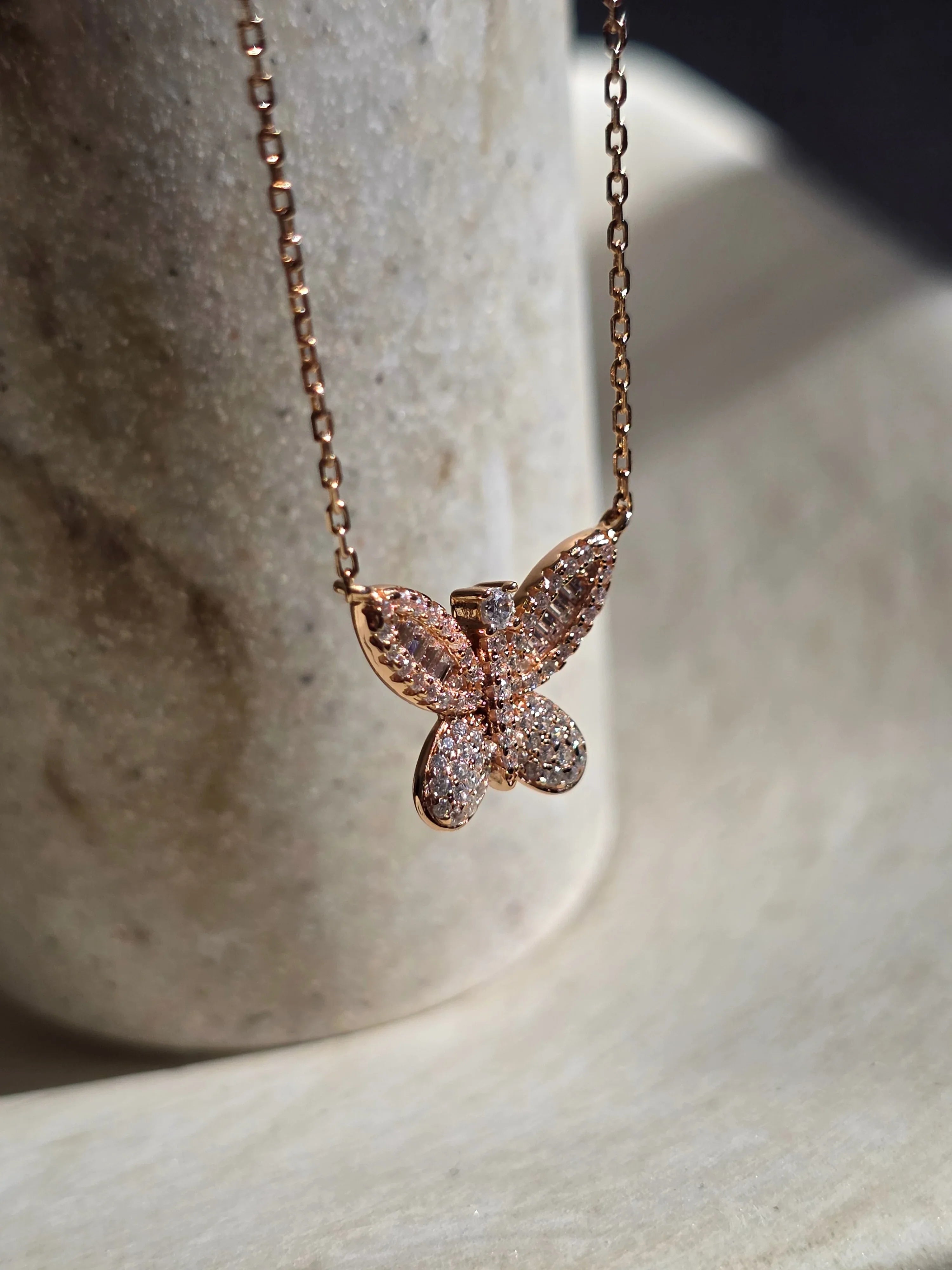 Rose gold butterfly necklace on a neutral background- side ways