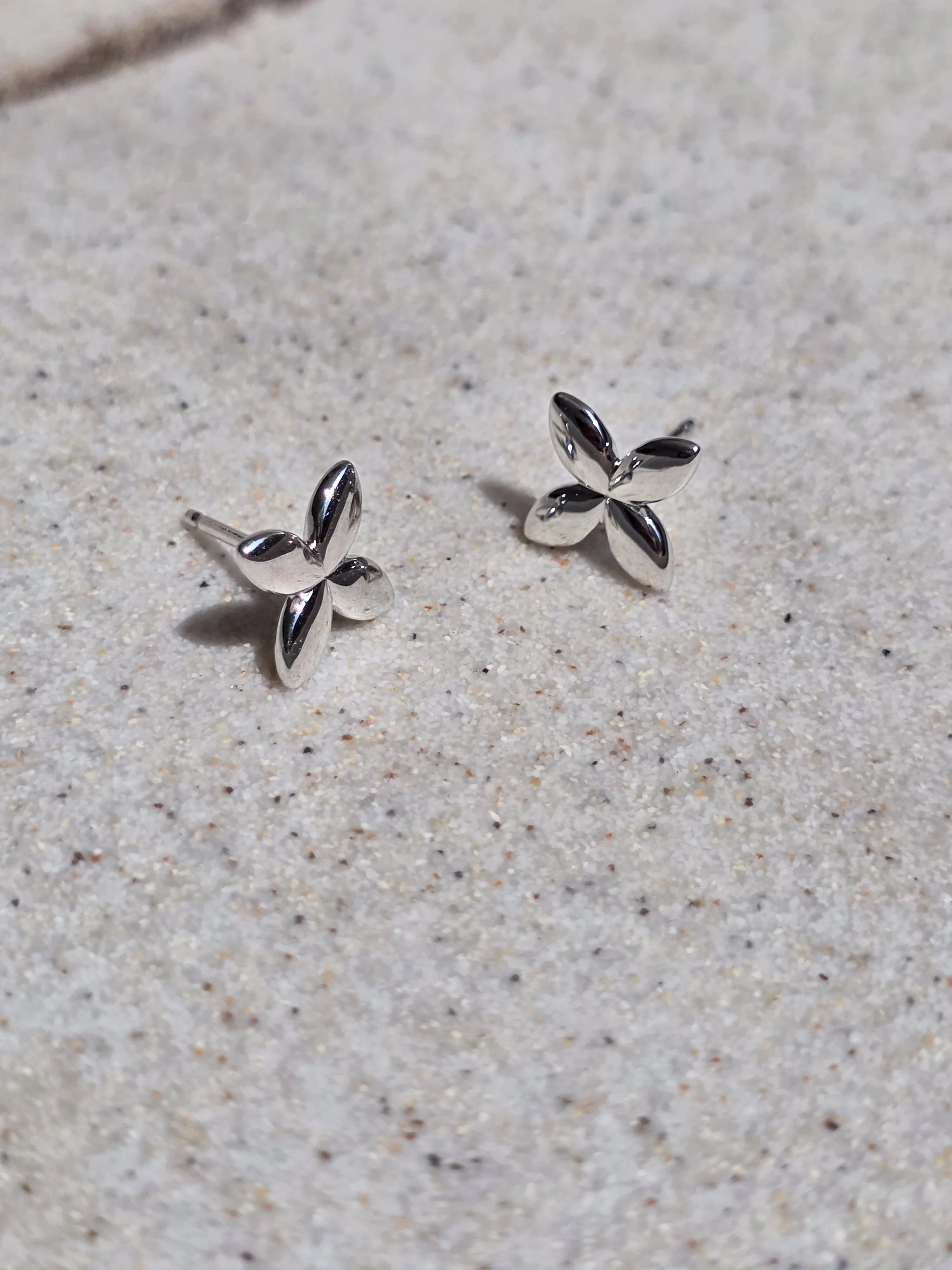 Silver flower-shaped earrings on a sandy surface- pair