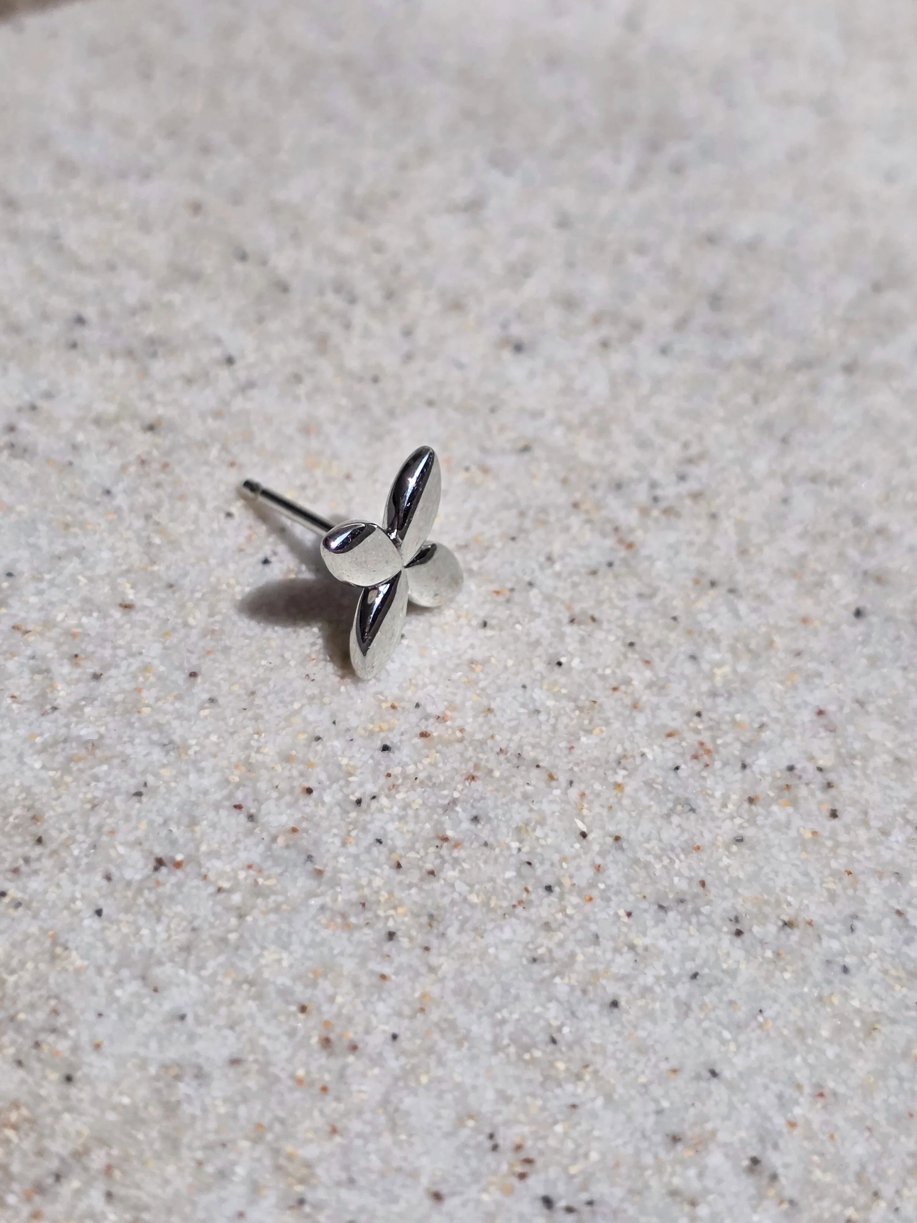Silver butterfly earring on a textured beige surface- front