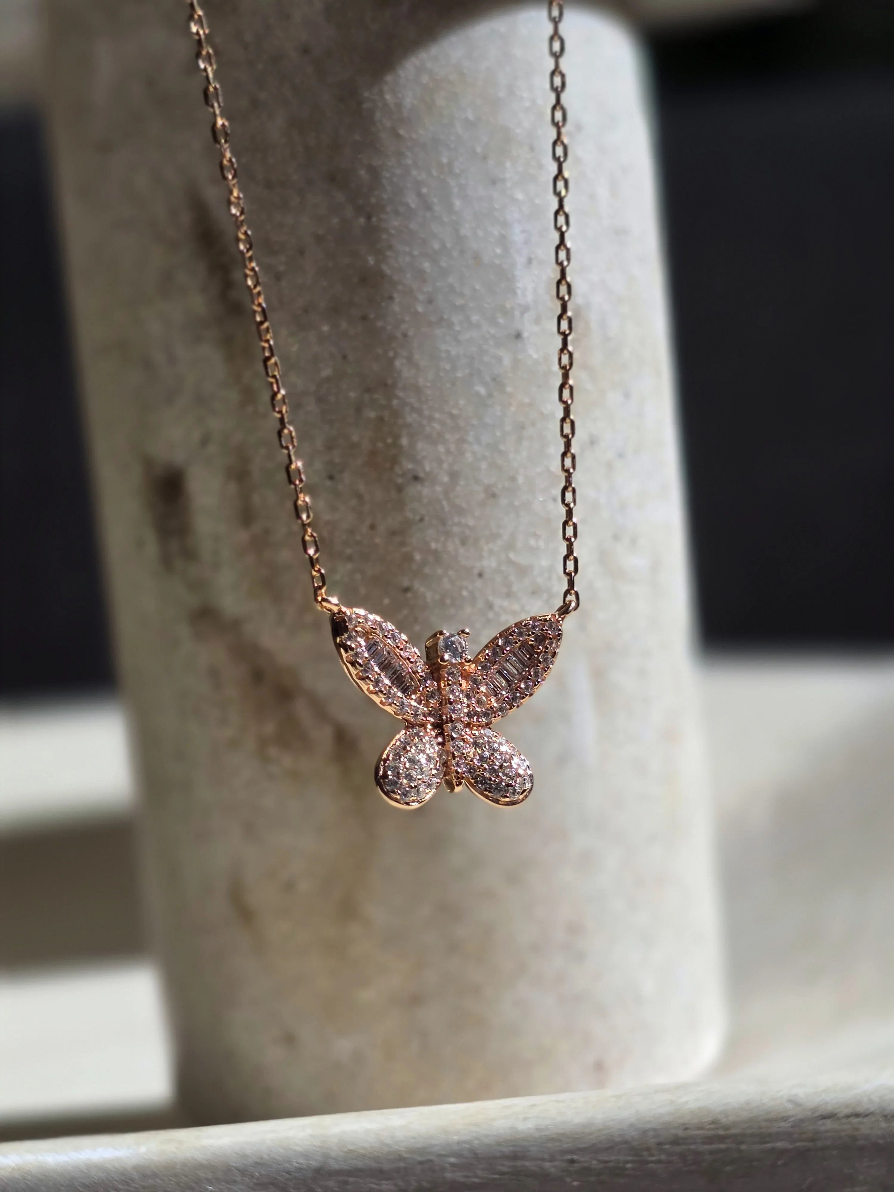 Rose gold butterfly necklace on a stone surface- upper