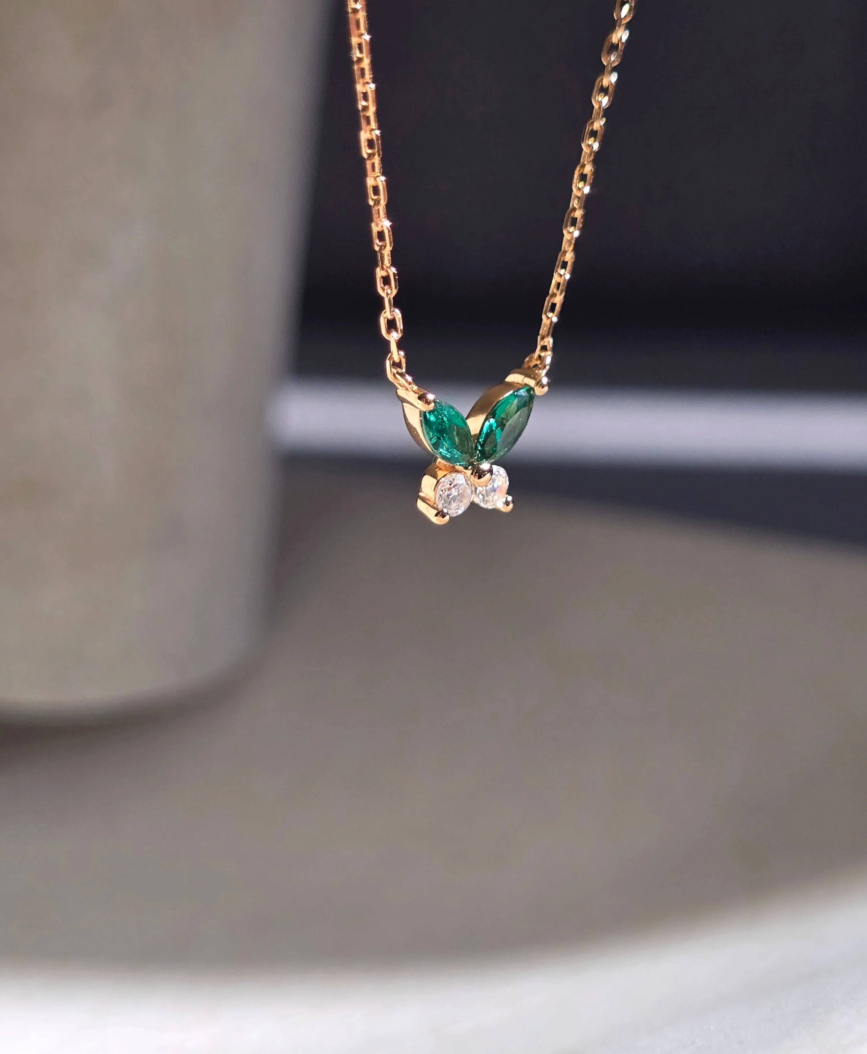 Gold necklace with green gemstones and a diamond on a neutral background- side ways