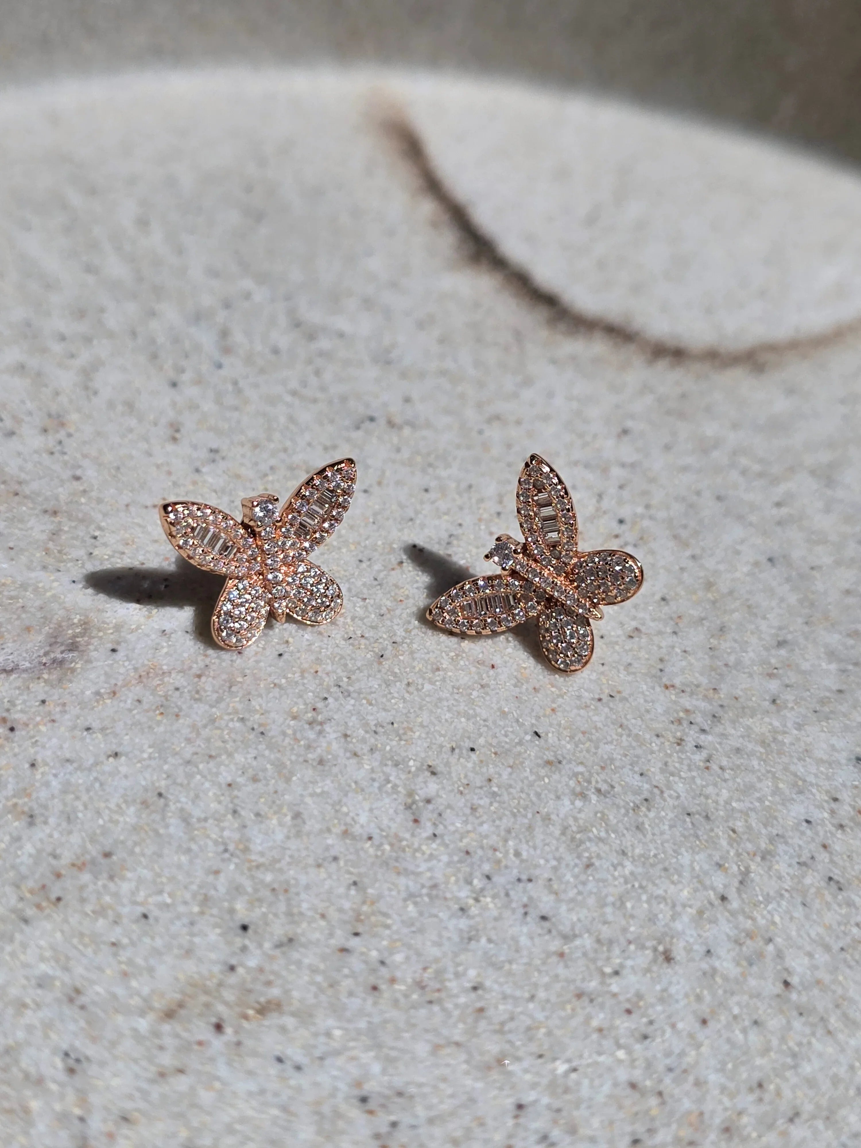 Rose gold butterfly earrings on a textured surface- pair